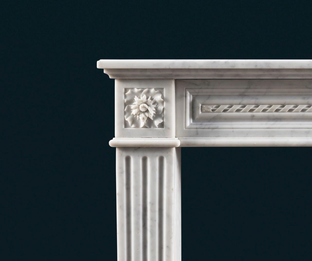 An elegant and petite mid nineteenth-century French Carrara marble fireplace surround in the Louis XVI style, with rope-twist carving to the centre of the panelled frieze, the flower-carved corner-blocks above fluted jambs. The jamb returns