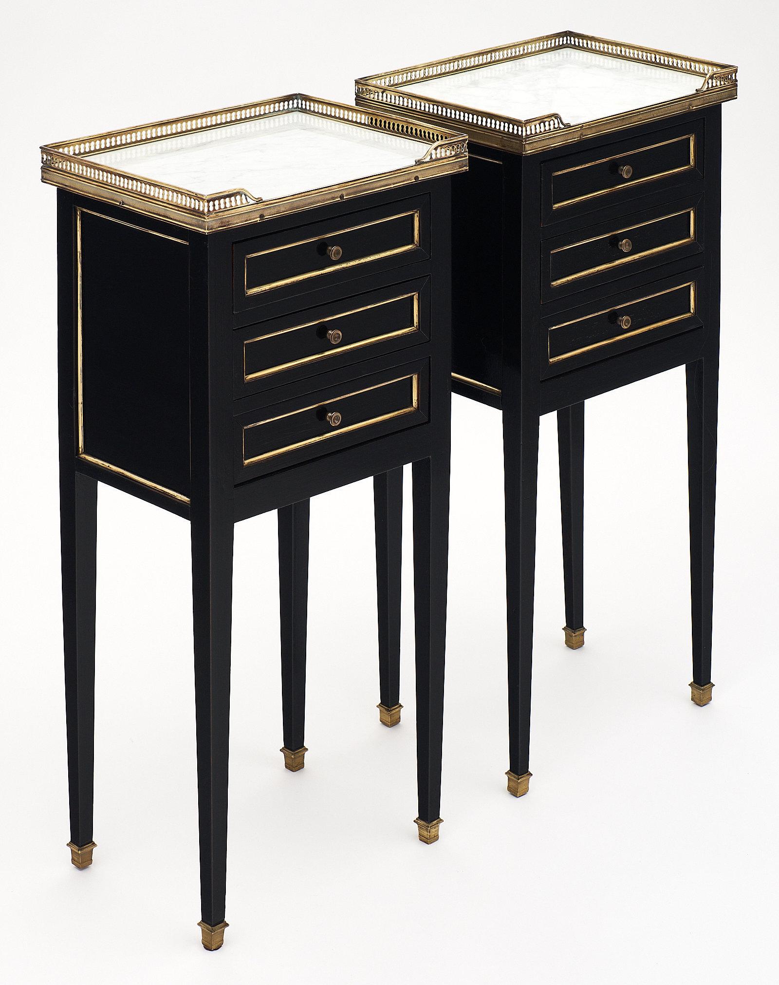 Carrara marble topped Louis XVI style side tables with brass gallery and trim. The mahogany tables have been ebonized and finished with a French polish for luster. The Carrara marble is original to the pair. We love the long tapered legs, and