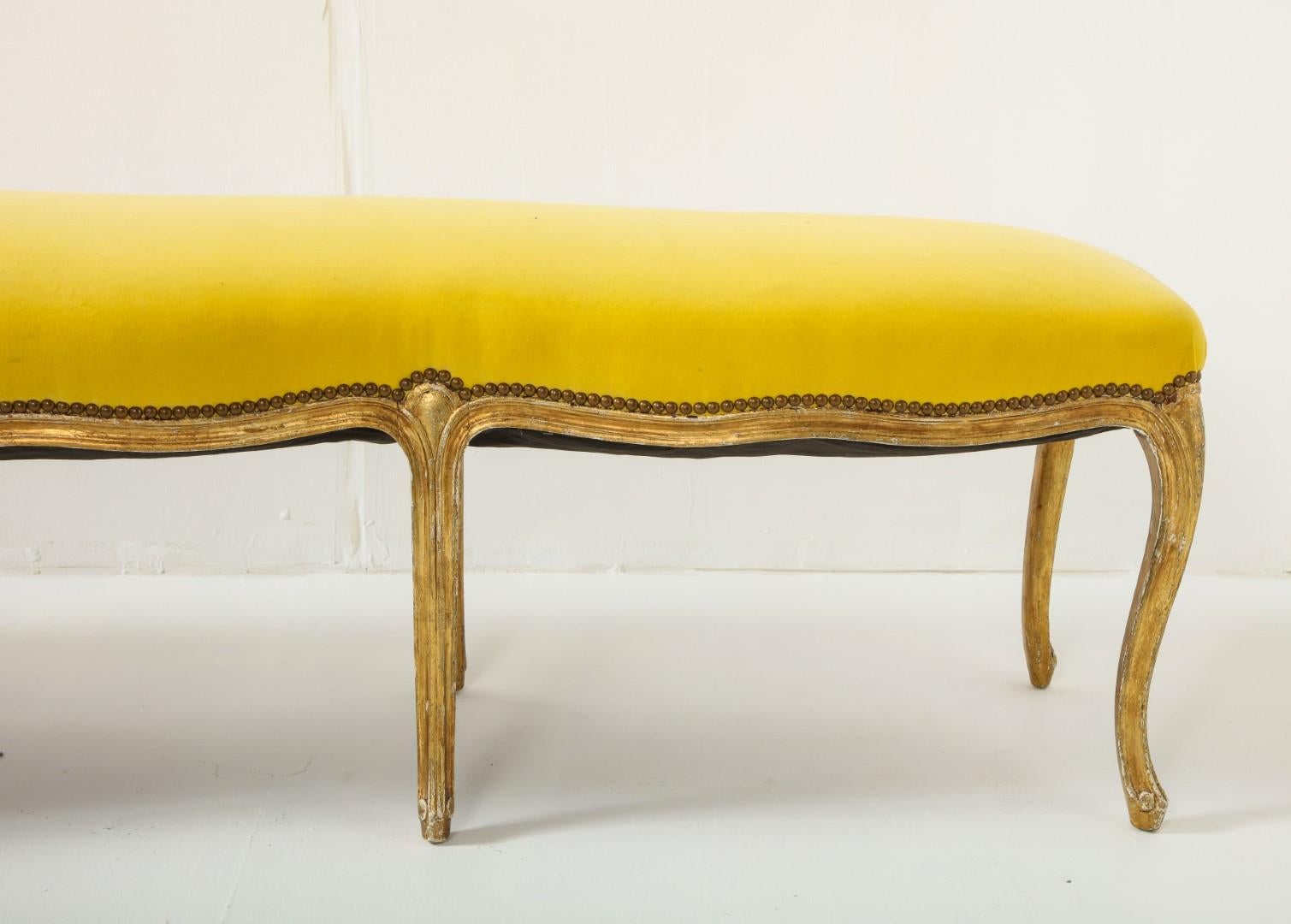 1930s French Louis XVI Style bench with carved and gilded cabriole legs. Top is recently upholstered in lemon yellow Kravet Versailles velvet, with brass nail head detail.