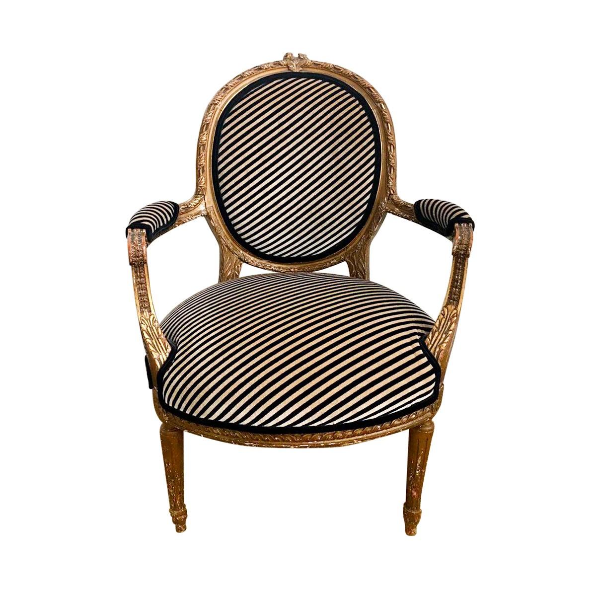 Early 20th century Louis XVI style carved giltwood armchair with round tapered legs. This oval back Fauteuil features beautifully carved acanthus leaf appointments and is newly reupholstered in a Lee Jofa beige/gold and black Oblique modern diagonal
