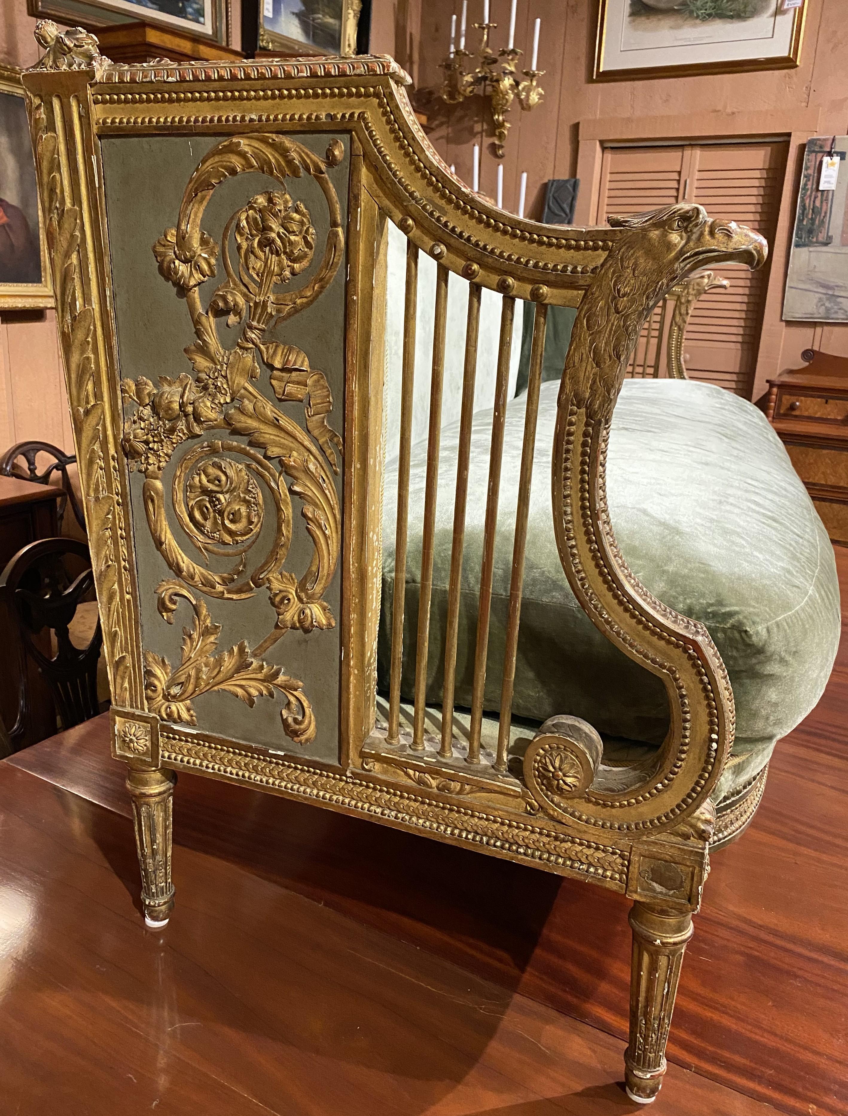 A fine example of a Louis XVI style giltwood settee with green upholstery, single seat pad,  carved crest rail, eagle form arms, scrollwork decoration, molding along the apron, side arm spindles, all supported by six carved round reeded tapered