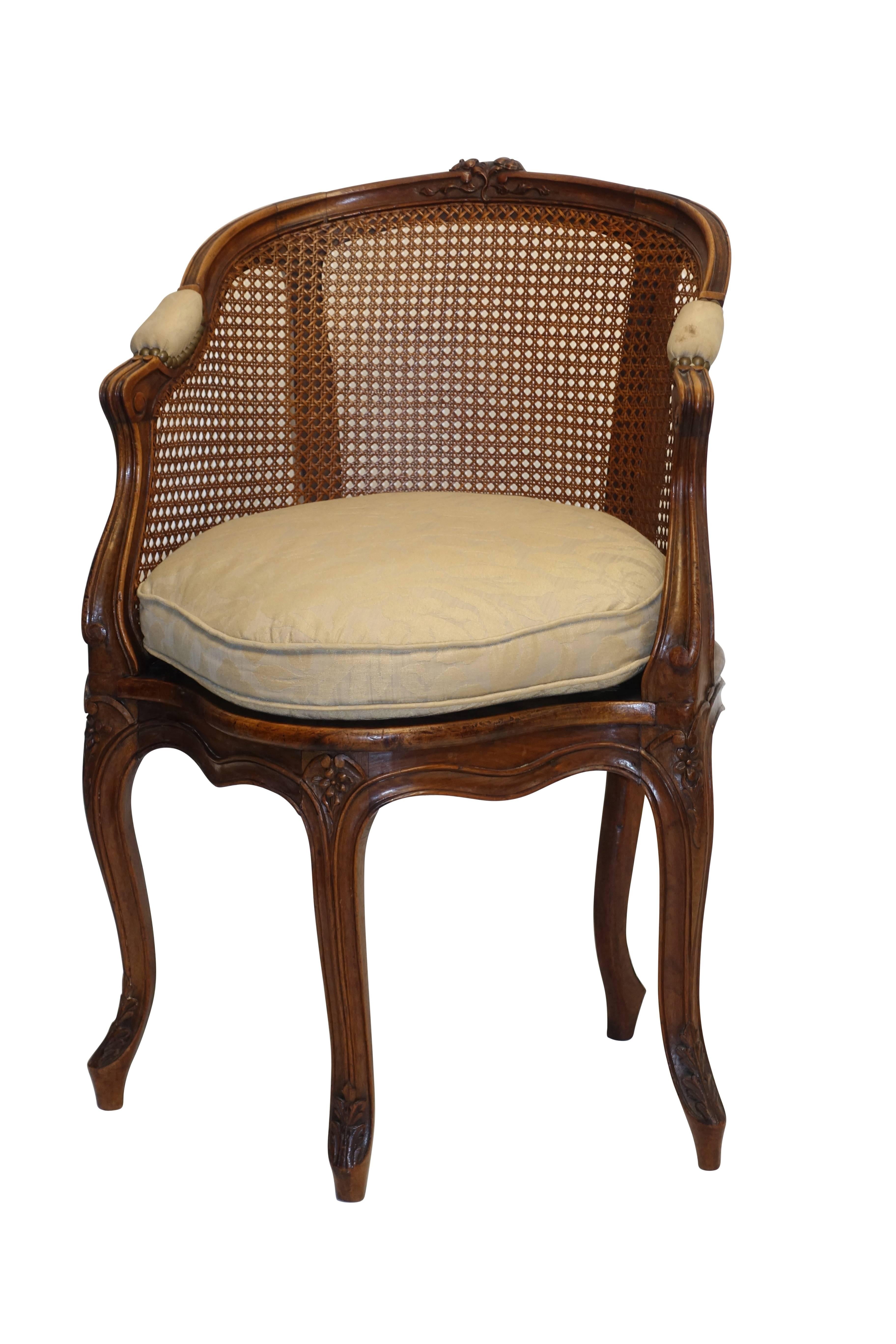 Louis XVI style hand-carved and caned walnut chaise de bureau with upholstered cushion. Carved floral and ribbon design at back rail and on the knees, standing on five cabriole legs ending in scroll feet, France, circa 1880.