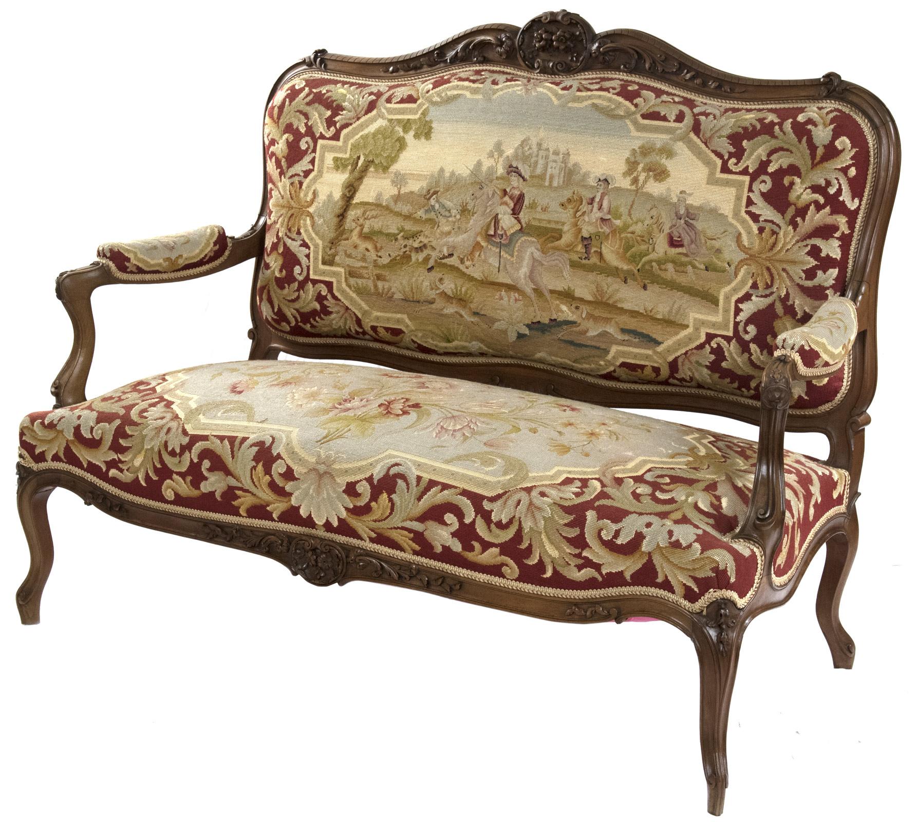 A Louis XV-style carved walnut sofa with gros point needlepoint upholstery in the style of Aubusson tapestry. The carved and shaped upholstered backrest, which depicts a hunting scene: men on horseback follow hunting dogs that are cashing a stag
