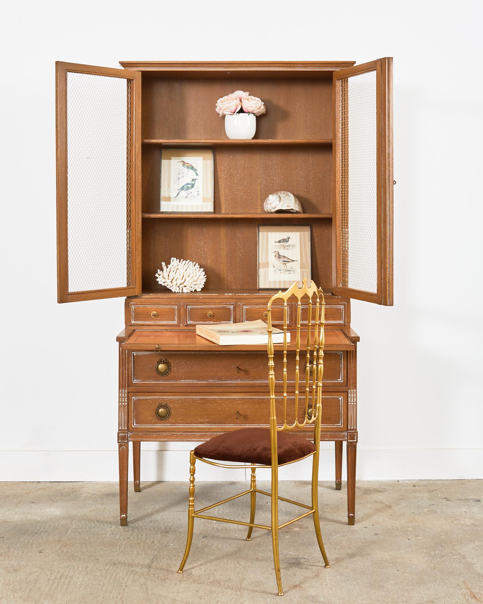 Fabulous French secretaire bookcase featuring a pull-out leather writing table or petite desk. Mid-century 2 part case crafted from oak. The chest is fronted by two large storage drawers with patinated brass ring pulls with a ribbon and bow motif.