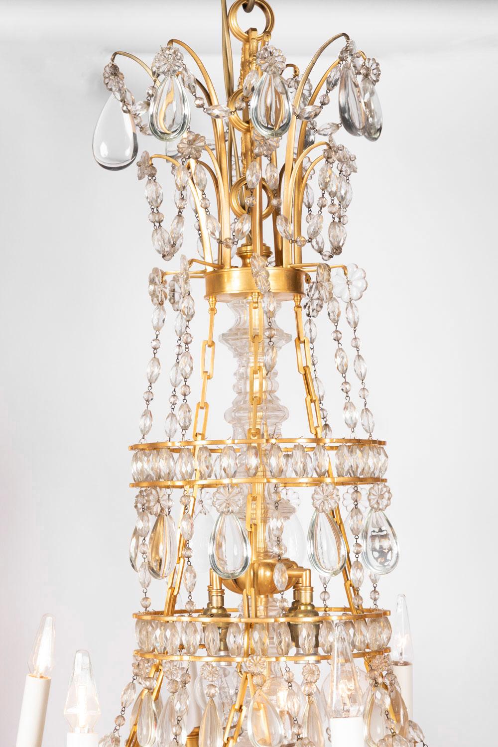 Louis XVI style chandelier, said Petit Trianon model with a gilt bronze structure and 8 fires. Model with a crowning supporting bronze rods slightly curved and fixed on a large gilt bronze ring on which 8 swags of crystal tassels in shape of