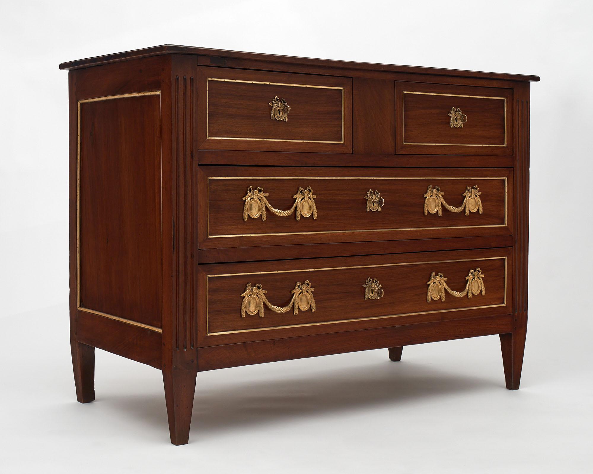 French Louis XVI style commode/chest. This piece is made of solid walnut and features tapered legs and wooden top. This classical chest boasts four dovetailed drawers and is adorned with finely gilded bronzes and gilt trims throughout.