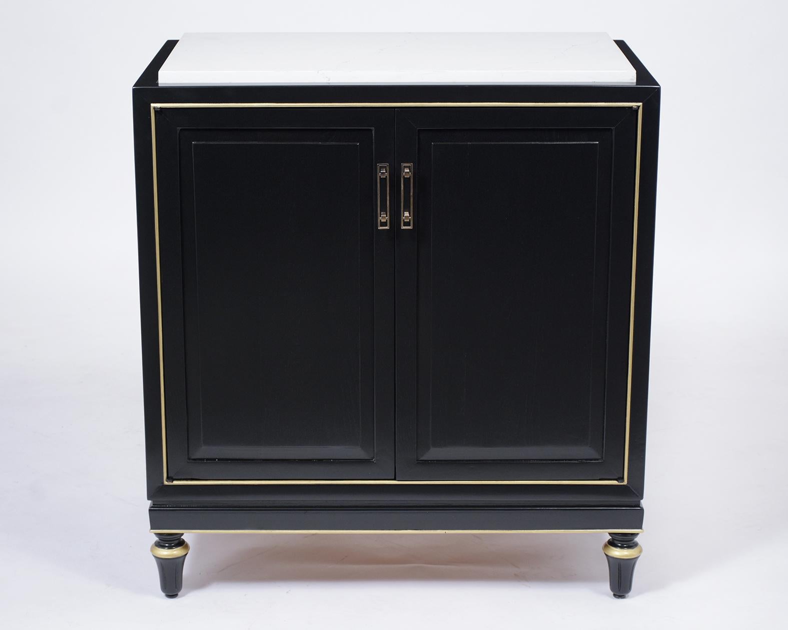 A fabulous Louis XVI style chest of drawers is handcrafted out of mahogany wood with a new ebonized lacquered finish and has been professionally restored. This cabinet features a white insert marble top, gilt molding accents, and two doors brass