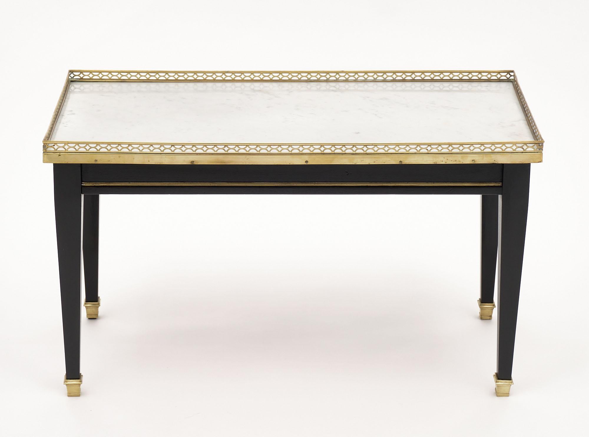 Coffee table from France in the Louis XVI style. This table features four tapered legs, a dovetailed drawer, and the original Carrara marble top. It is enhanced by the gilt brass gallery, bronze feet, and gilt brass trims. The wood has been finished