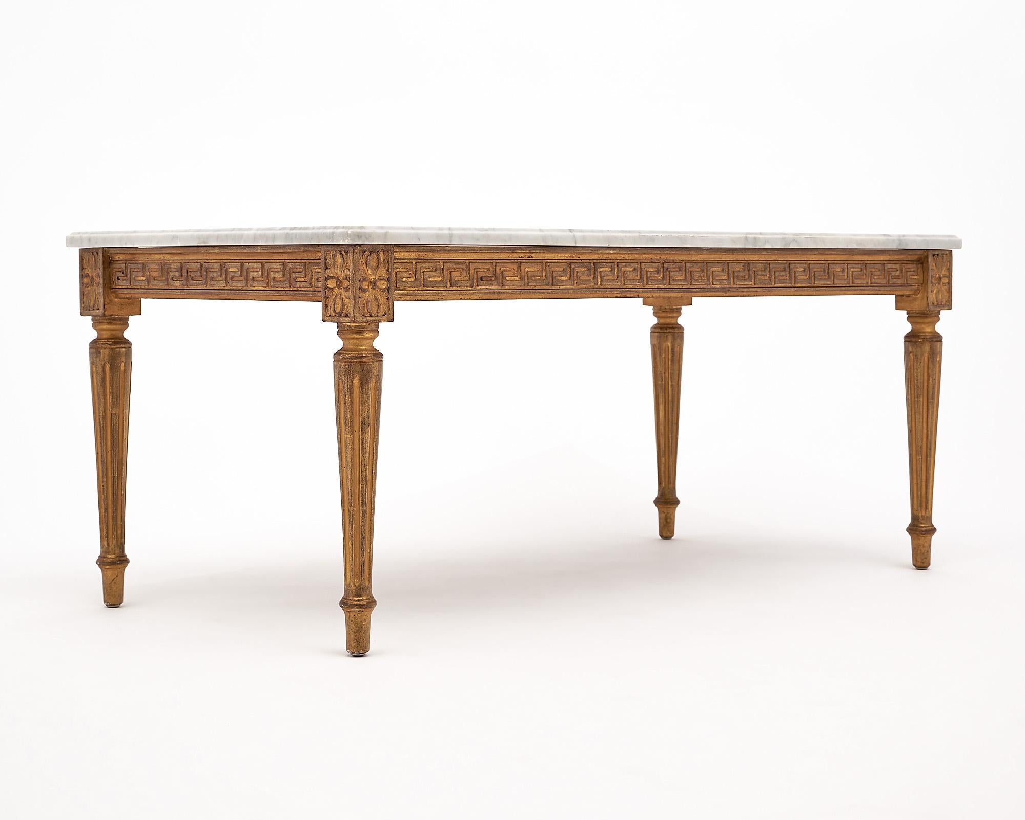 Coffee table, French, in the Louis XVI style. This piece is made of hand carved wood with a Greek key design frieze on the apron. The legs are tapered and fluted. The base has 24 carat gold leafing throughout. This neoclassical table is topped with