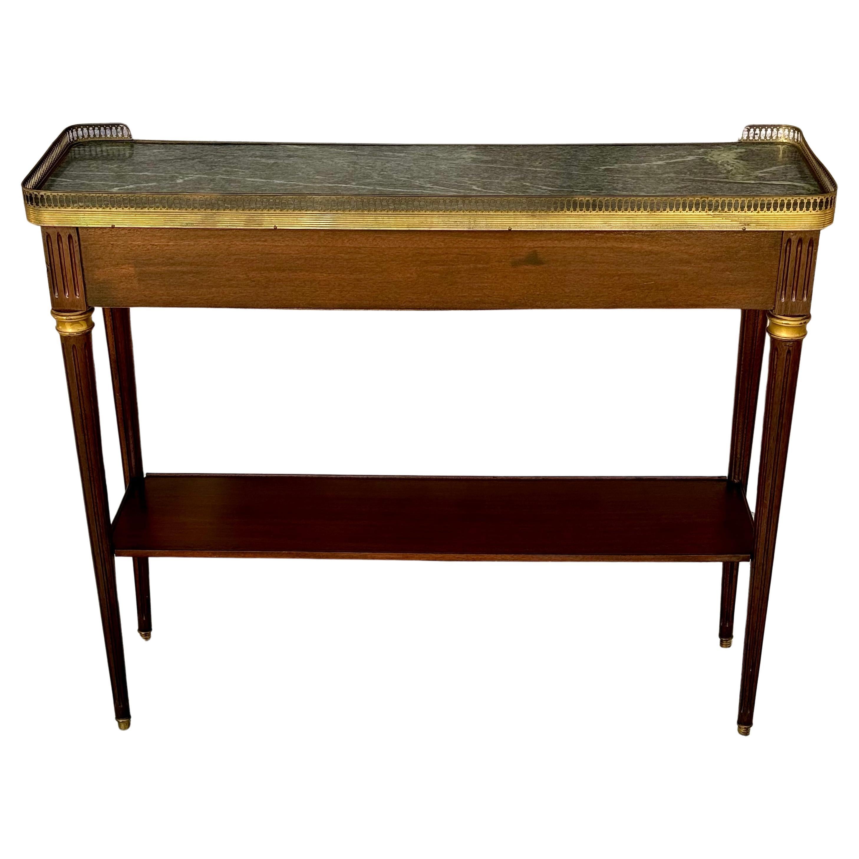 . Early 20th Century Louis XVI style marble top console dessert table with marble top and brass gallery. Table features two drawers and stands on four tapered and fluted legs. Feet with brass sobots.