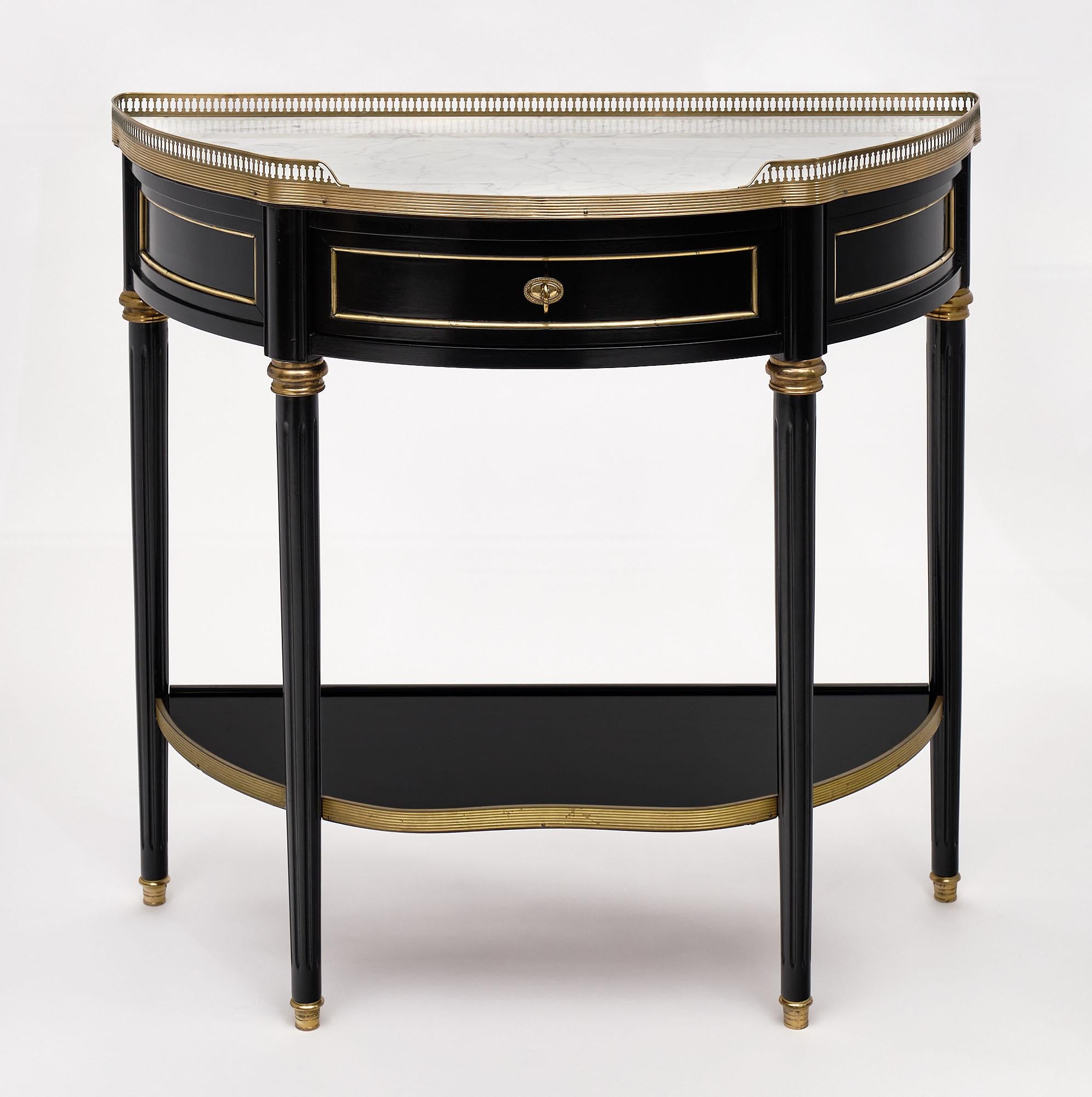 Console, French, “demilune” in the Louis XVI style featuring an intact Carrara marble top and opened brass gallery. There is gilt brass trim throughout. We liked the single drawer in the apron of this elegant piece. The wood has been ebonized and