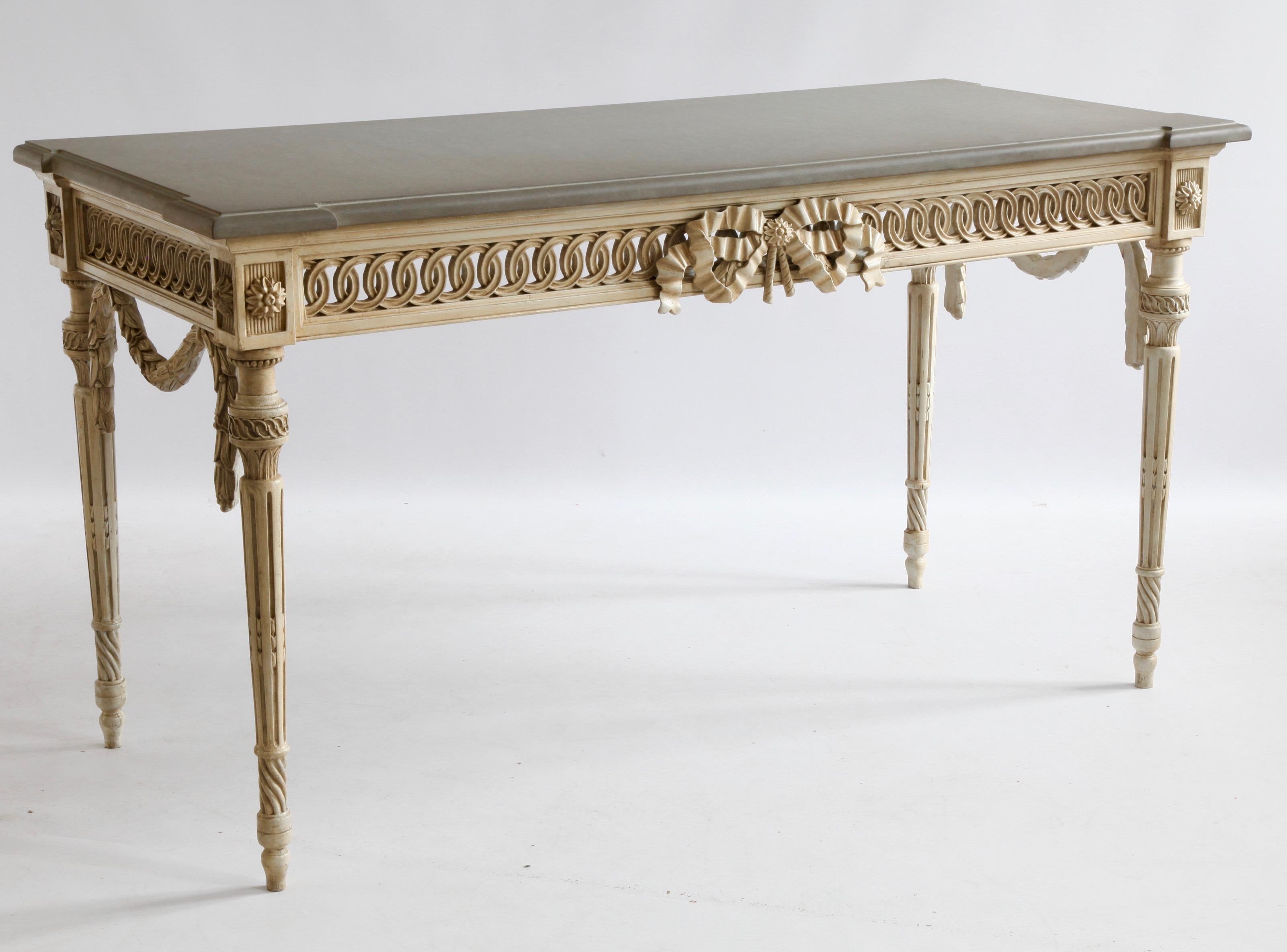 A freestanding console table hand carved in the Louis XVI style with fine, period detailing and hand finished in an aged, French grey patina created using traditional methods and materials. The piece is complemented with a grey stone, beveled top