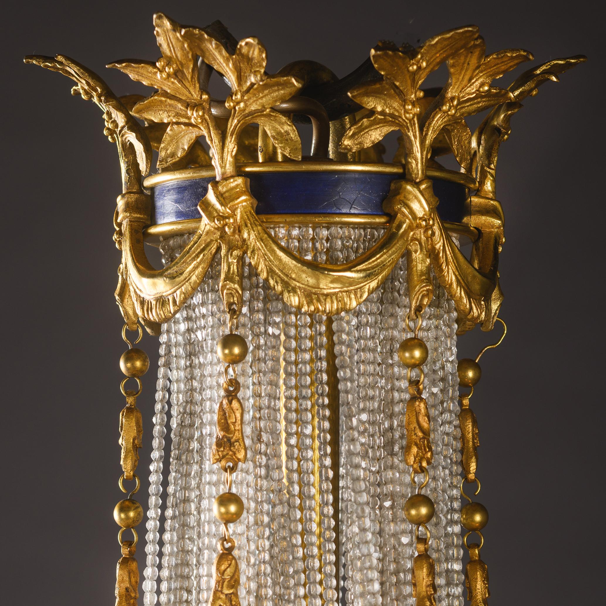 Fino candelabro de carpa y armazón de bronce dorado y cristal tallado, estilo Luis XVI, con galerías esmaltadas en azul. 

La corona del candelabro tiene forma de banda esmaltada en azul con guirnaldas de bronce dorado y motivos foliados de la que