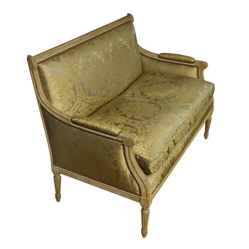 A Louis XVI style damask upholstered and carved settee. The settee seamlessly blends opulence and sophistication crafted with a carved wooden frame that exemplifies the grandeur of the 18th-century French design. The timeless damask pattern of the