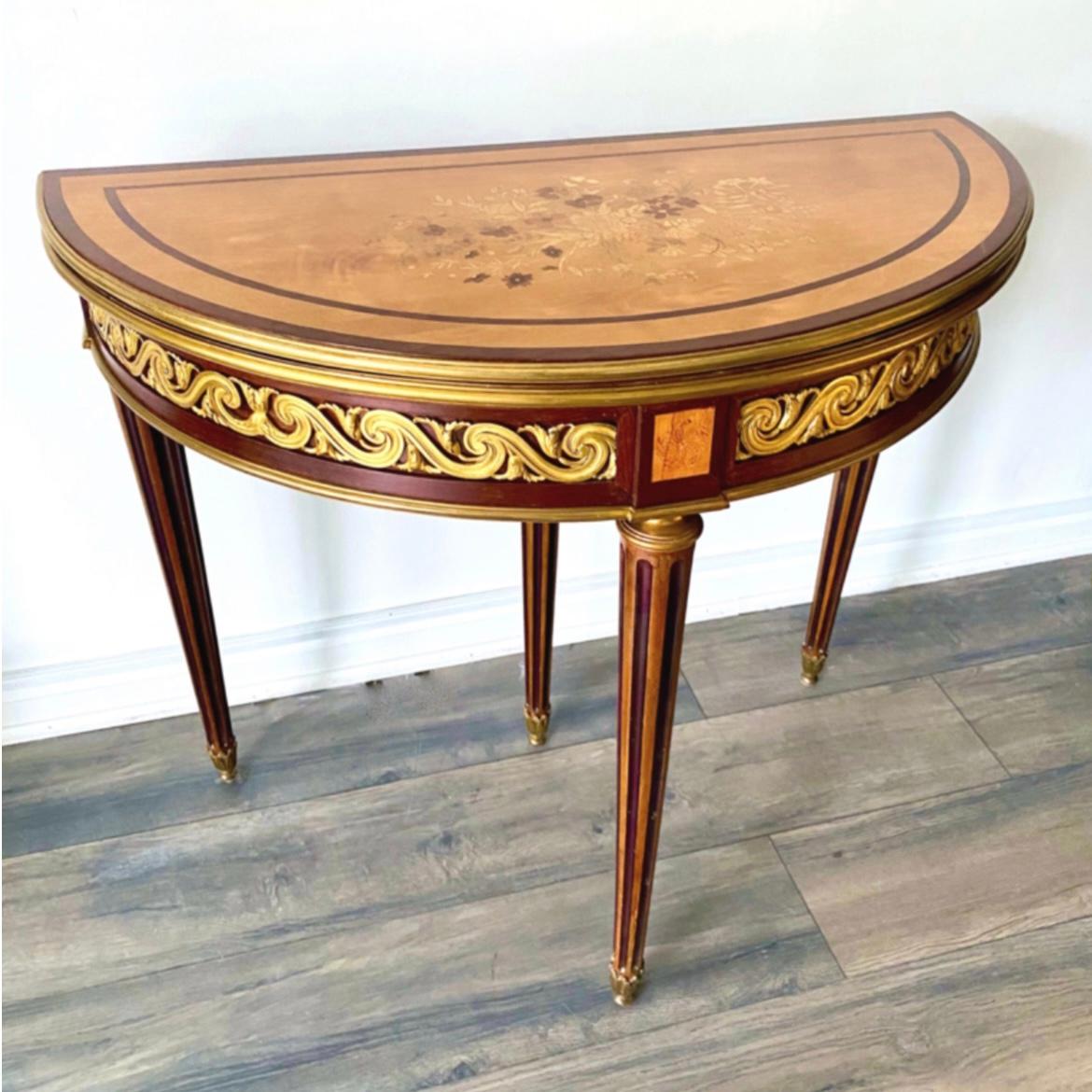 Our demi-lune table in the Louis XVI has a top with beautiful floral marquetry inlay, frieze with gilt bronze Vitruvian scroll motif, hand-painted fruitwood rosettes, fluted legs with bronze feet. 29.75 inches tall and 35 inches wide and 17.5 inches