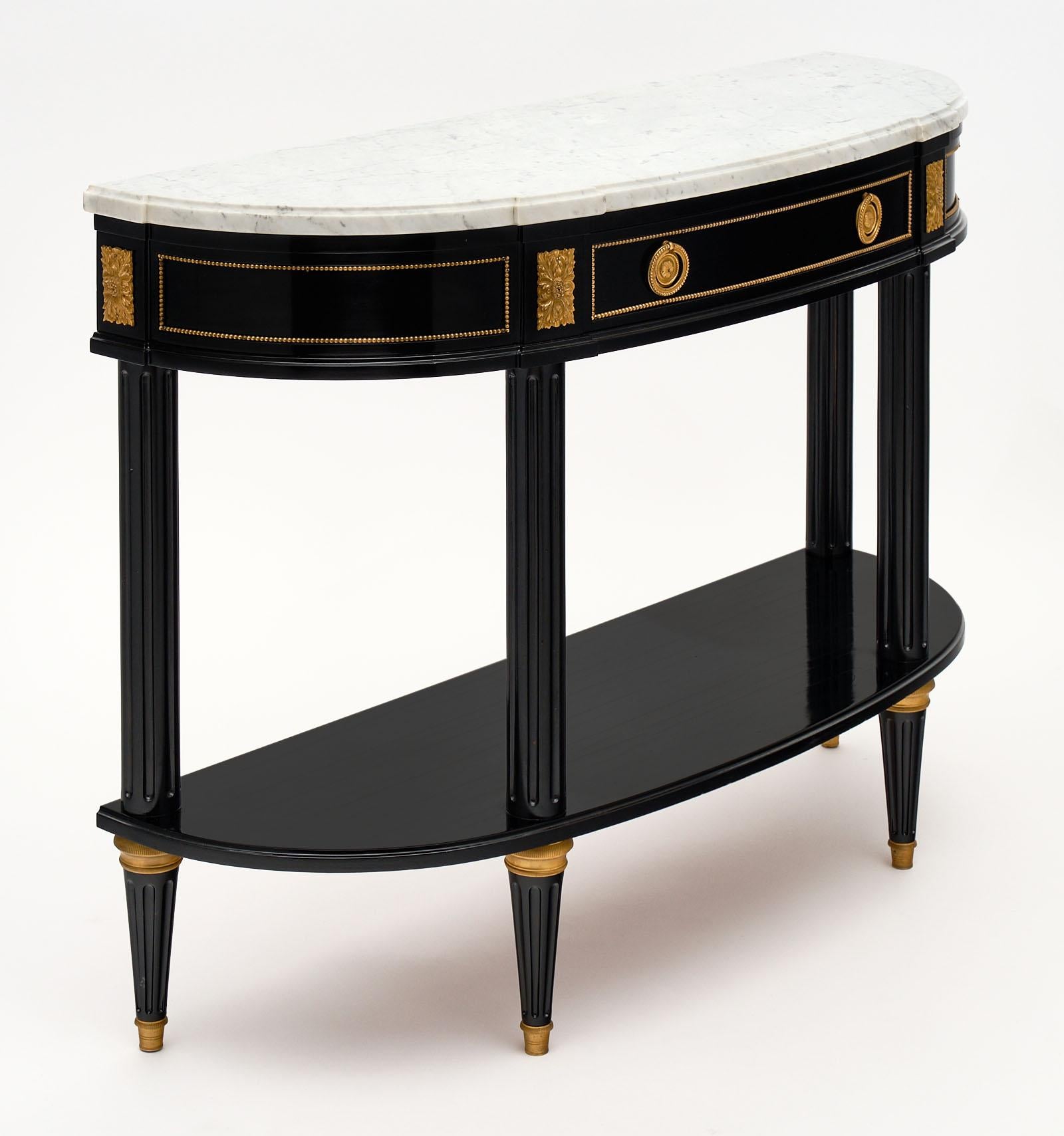 Louis XVI style demilune console table from France with a white Carrara marble slab top. The gilt brass trim and hardware throughout is original and brings a classic elegance to the piece. It has been finished with an ebony French polish for a