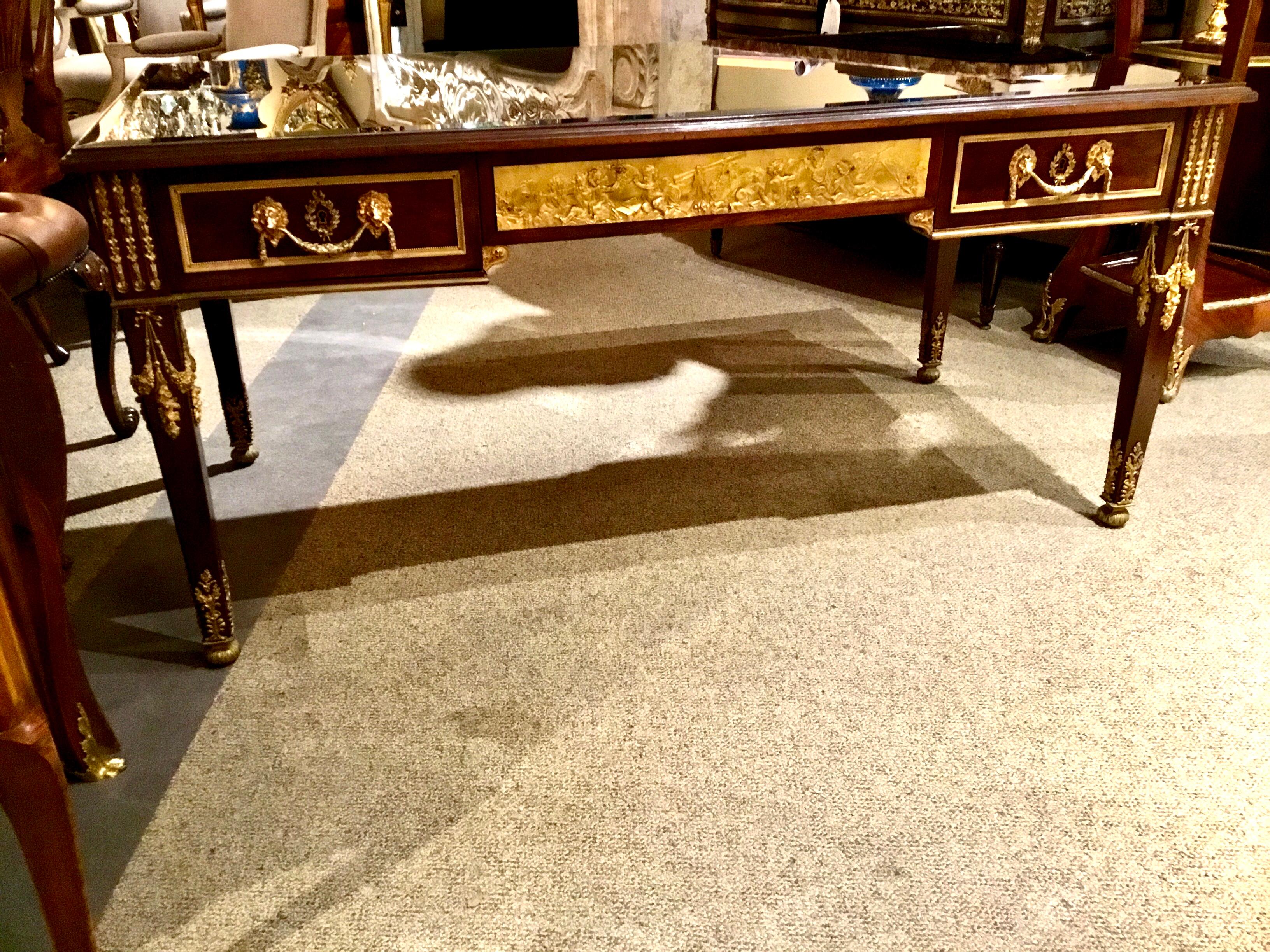 Late 19th century, the rectangular top with an inset leather writing surface within a molded edge and
Topped with a new piece of beveled glass, above a conforming frieze fitted with one side with
A central drawer with an applied ormolu plaque,
