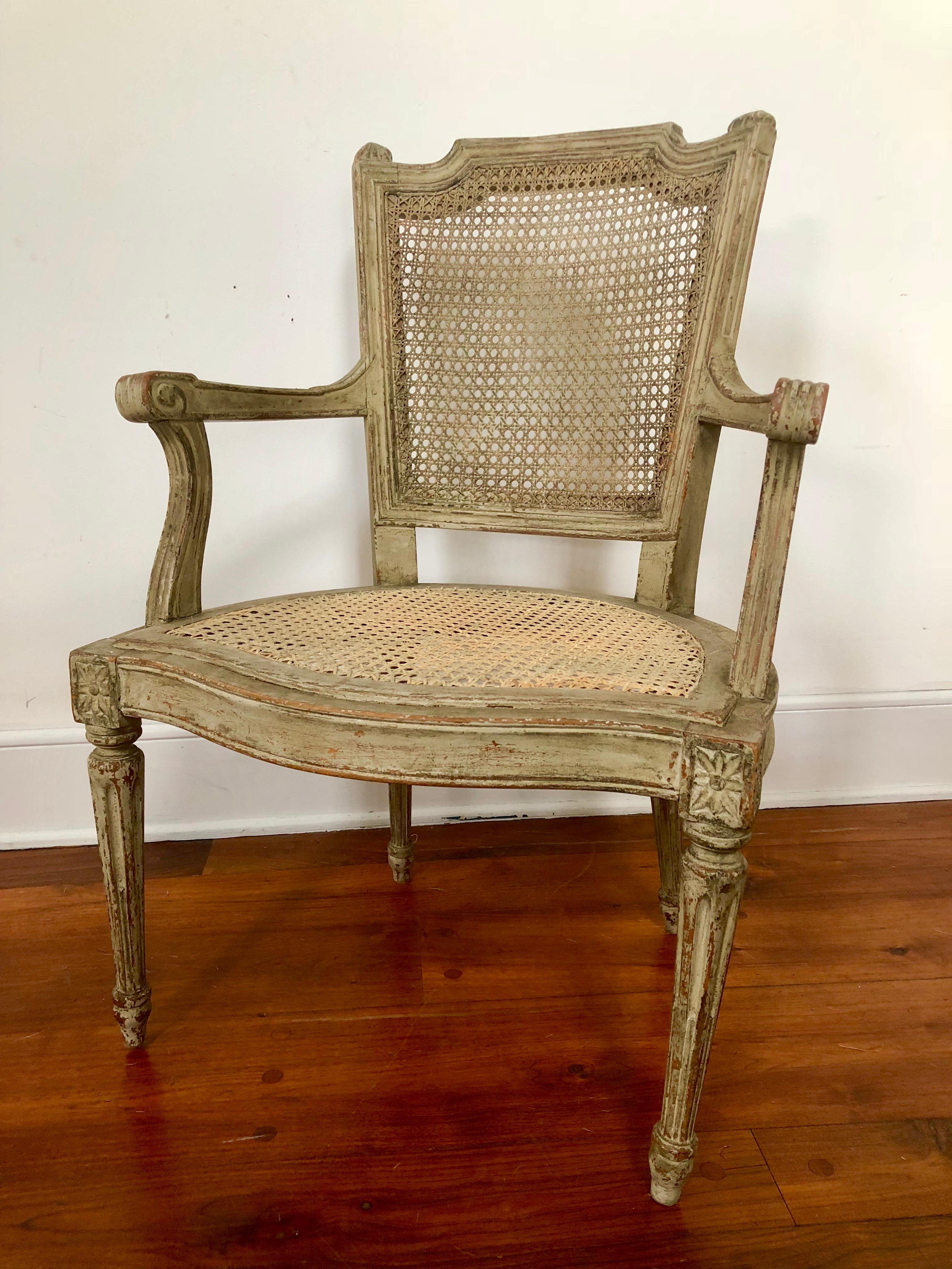 A French Louis XVI Style “fauteuil de bureau” in grey/ green painted finish with caned seat and back, early 20th century.