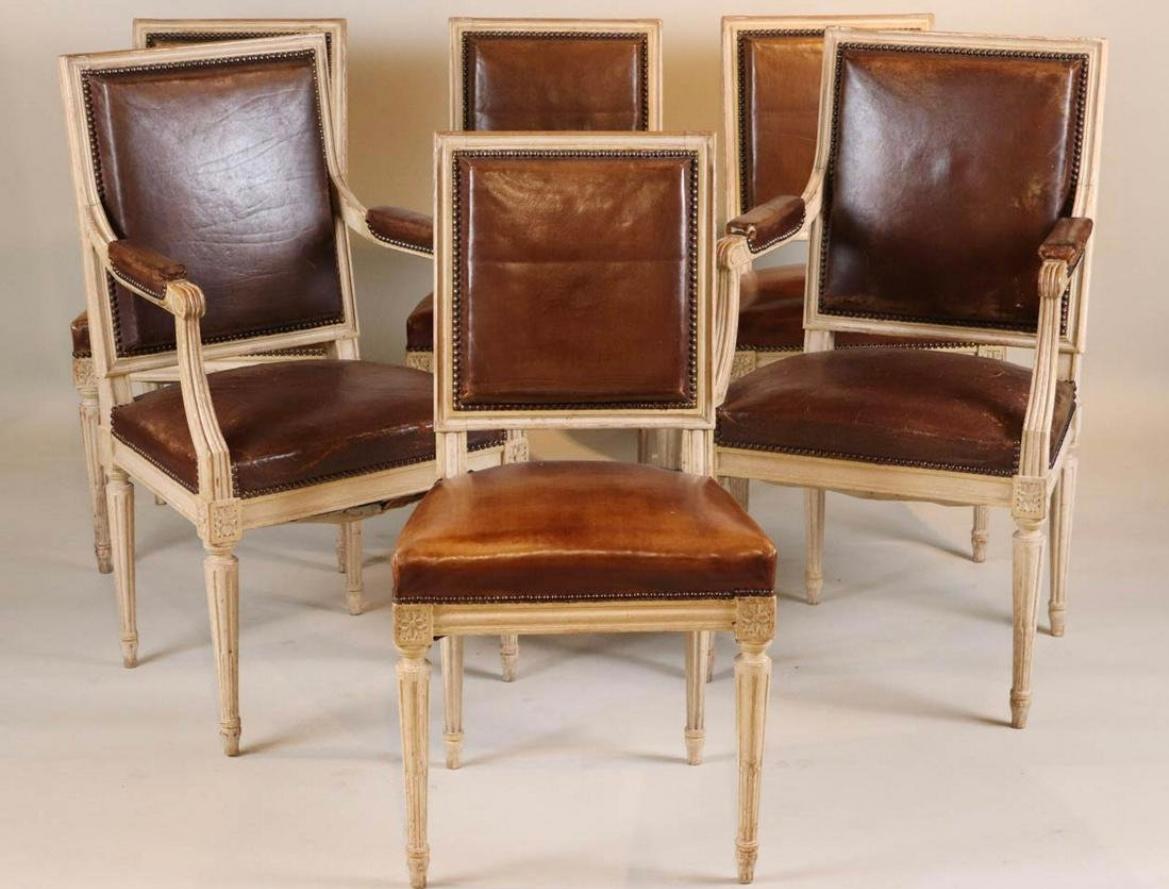 A stunning set of 6 Louis XVI style dining chairs in beech, with a distressed painted finish, upholstered in brown leather with a lovely patina. A pair of armchairs and four side chairs. 