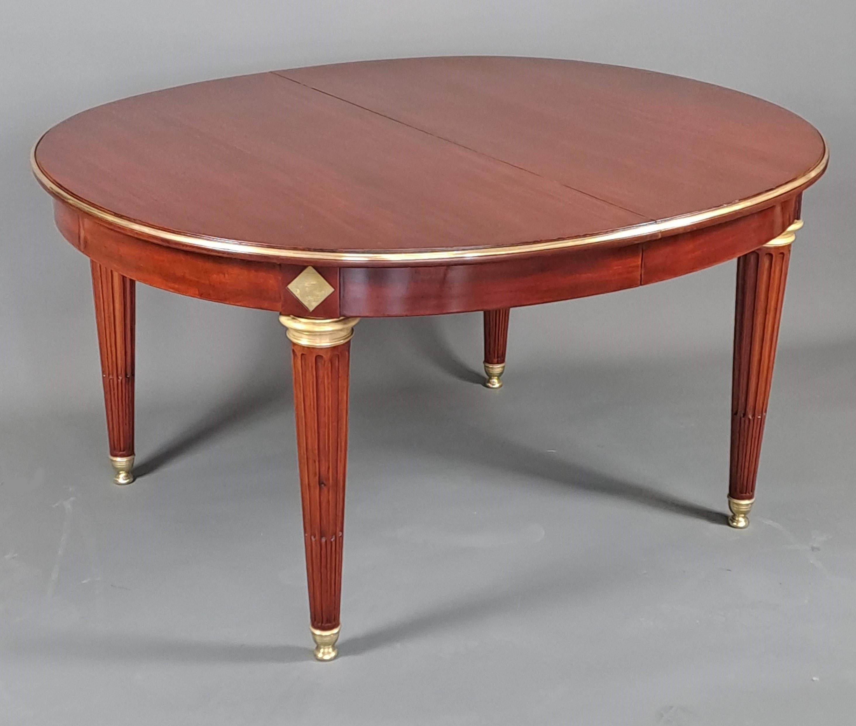 Beautiful oval table in solid mahogany and mahogany veneer in Louis XVI style. Four solid feet with rough grooves decorated with gilded bronze shoes and rings. On the headband we find diamond-shaped scrapers above each foot. The oval tray is