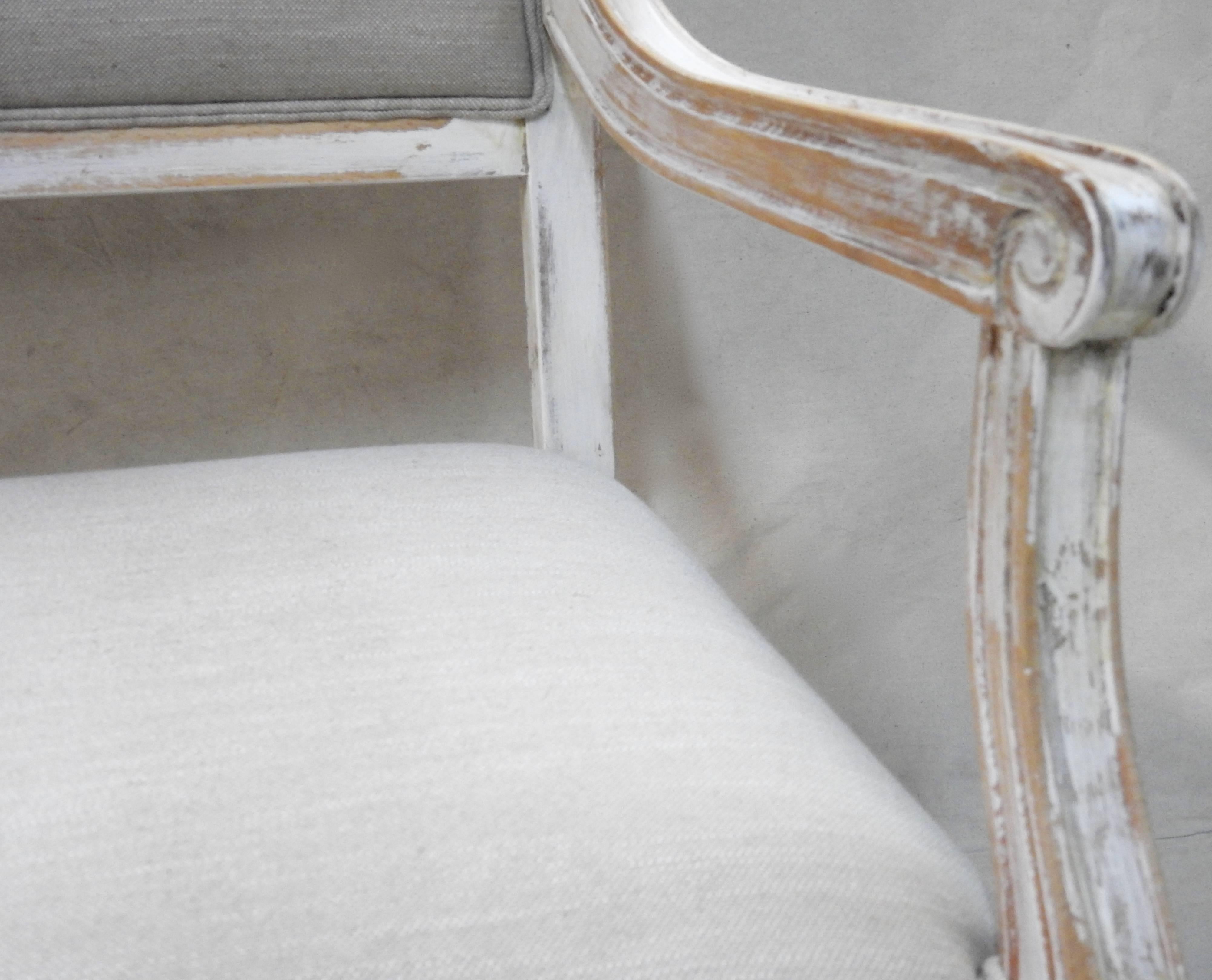 We are offering a superb Louis XVI style hall bench settee. It has a painted and distressed finish, featuring disrupted white and lead white colors with some of the wood showing through. The angular framed back and tight seat are upholstered in a