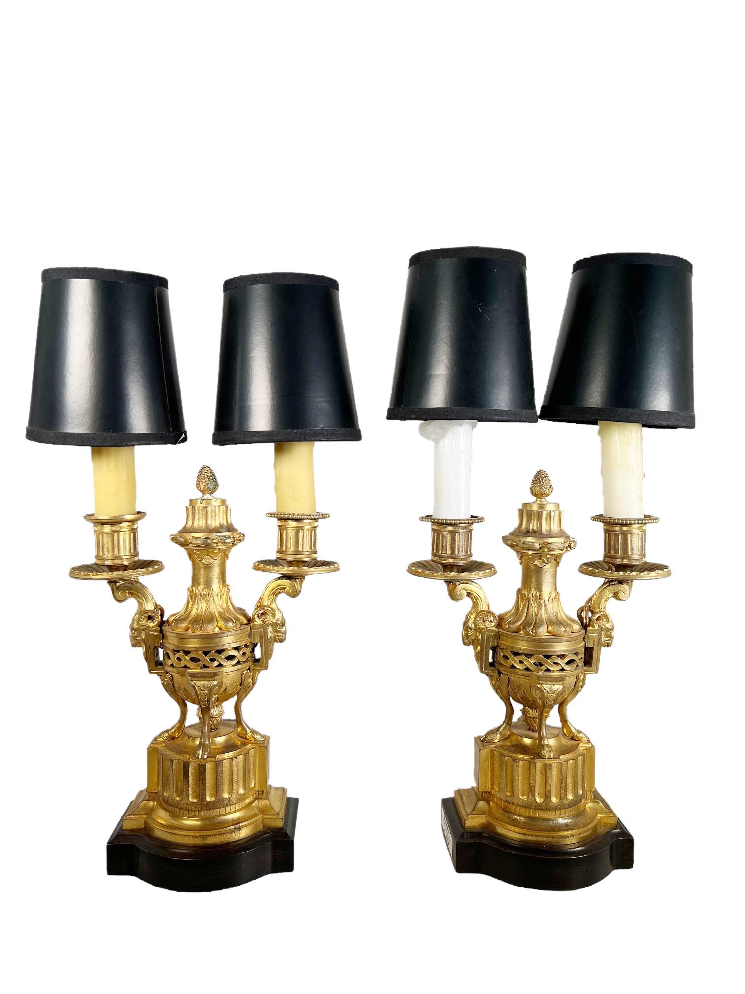 A pair of Louis XVI bronze dore candelabra raised on custom wood bases. Very fine quality bronze dore with open work in the center with rams heads on the side. Black shades. Circa 1890, France. Nine and a half inches to top of candle holder.