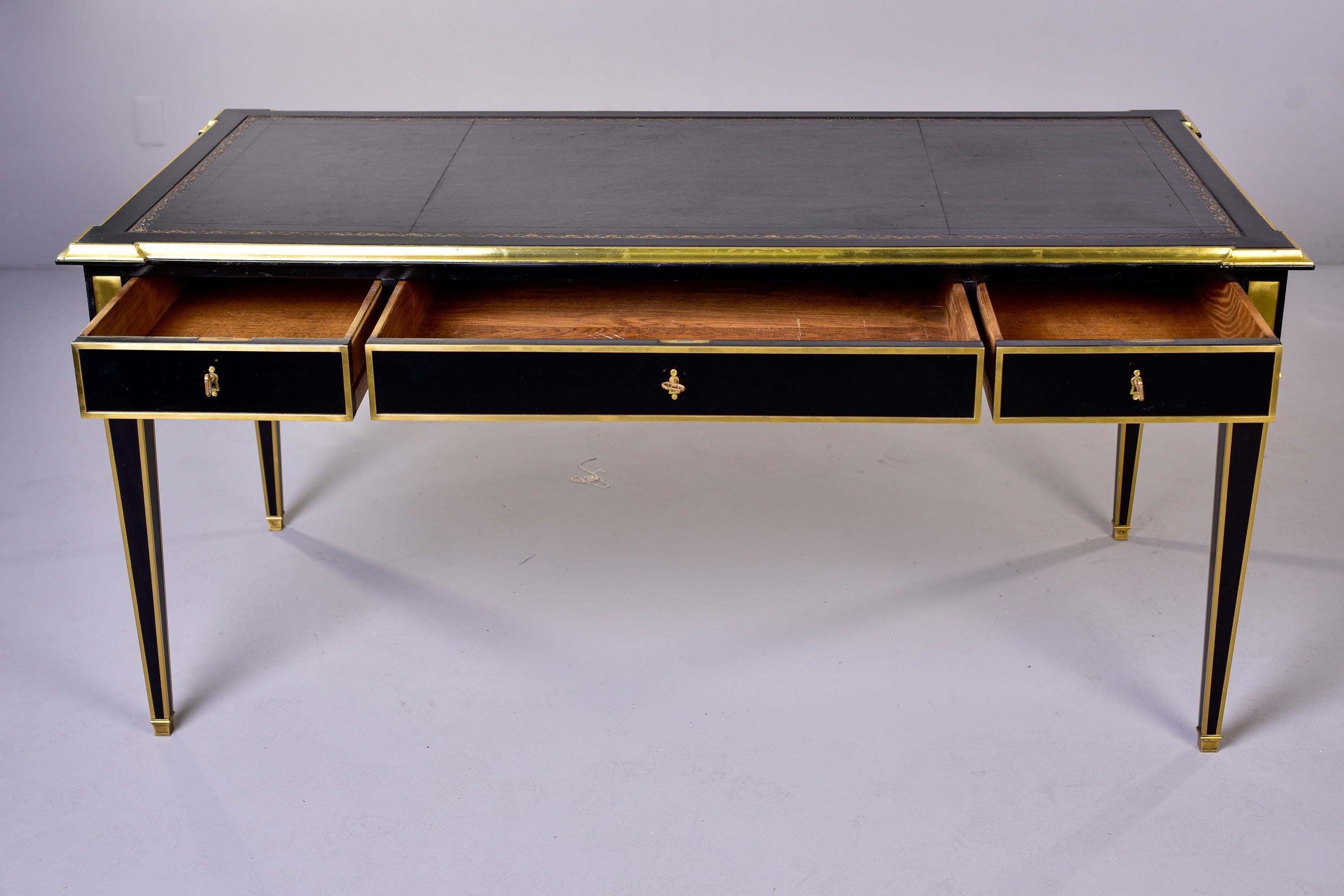 Circa 1860s Louis XVI style desk is finished and trimmed in brass on both sides. Front of desk has three functional locking drawers; back of desk has faux drawers. Both sides have leather-topped pull-out extendable work surfaces. Tapered legs with