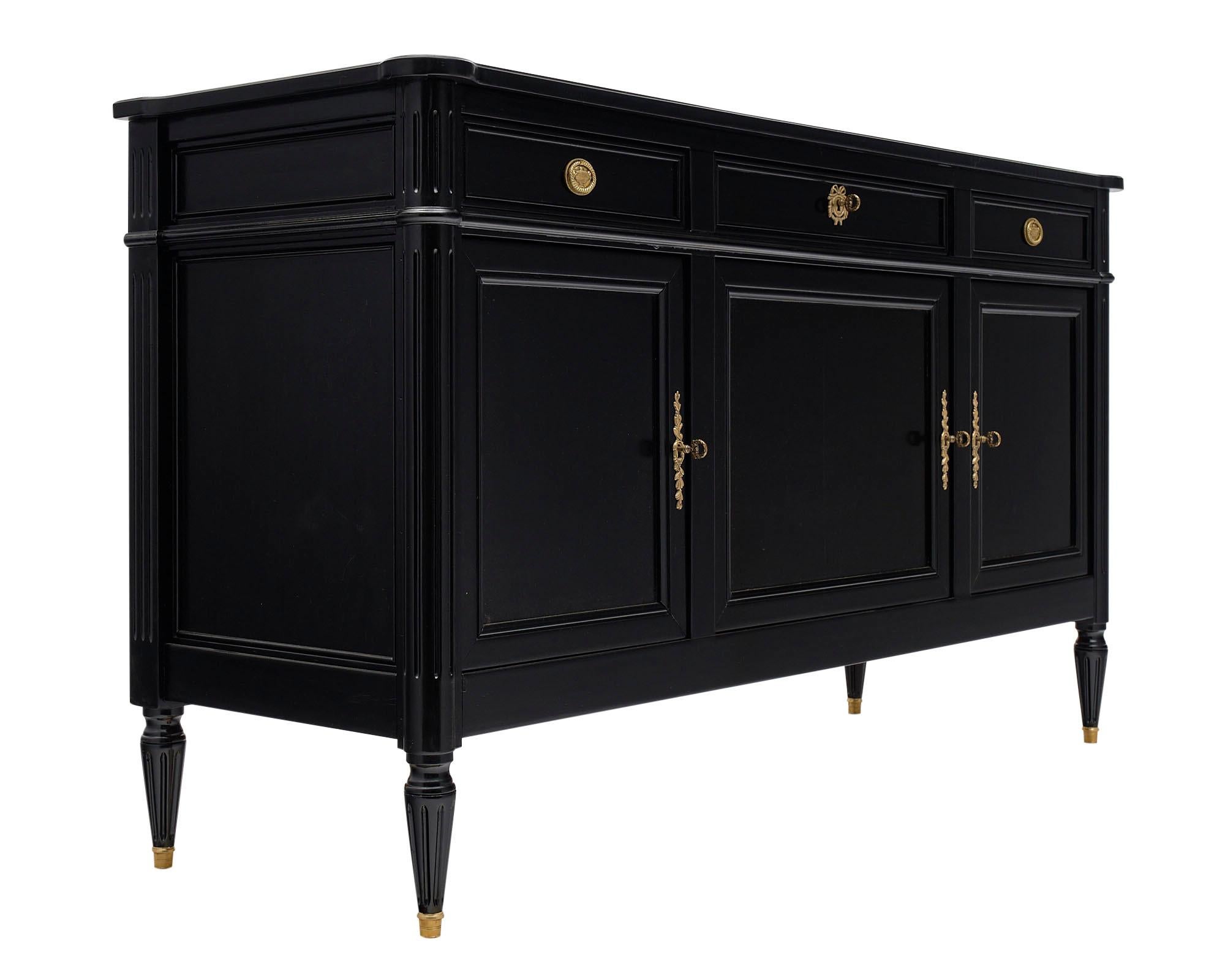 Louis XVI style ebonized buffet made of mahogany and finished with a French ebonized and lustrous polish. There are three dovetailed drawers above three doors that open to adjustable shelving. We love the brass hardware original to the piece and the
