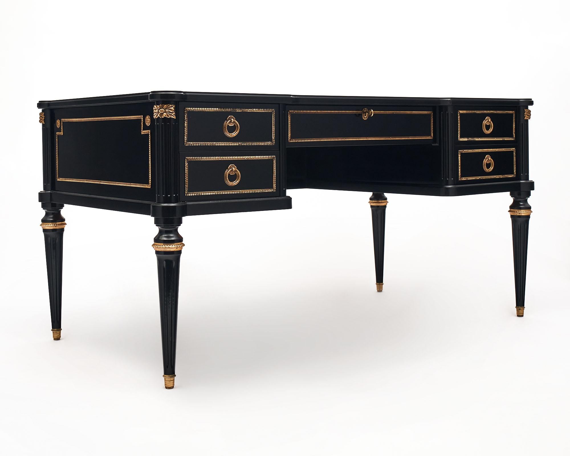 Desk from France in the Louis XVI style. This antique piece has been ebonized and finished with a lustrous French polish. The top has a black leather writing surface, featuring gold leaf trim. There are five dovetailed drawers each showcasing a gilt