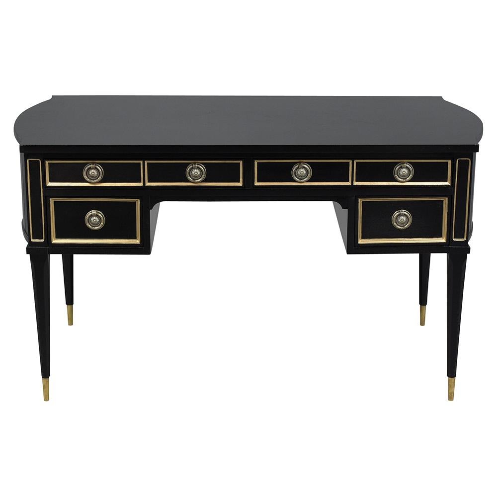 An elegant 1950's Louis XVI style desk that has been professionally restored, newly stained in a rich ebonized color with gilt details and a newly lacquered finish. The writing table features five drawers framed by gilt molding with brass handles