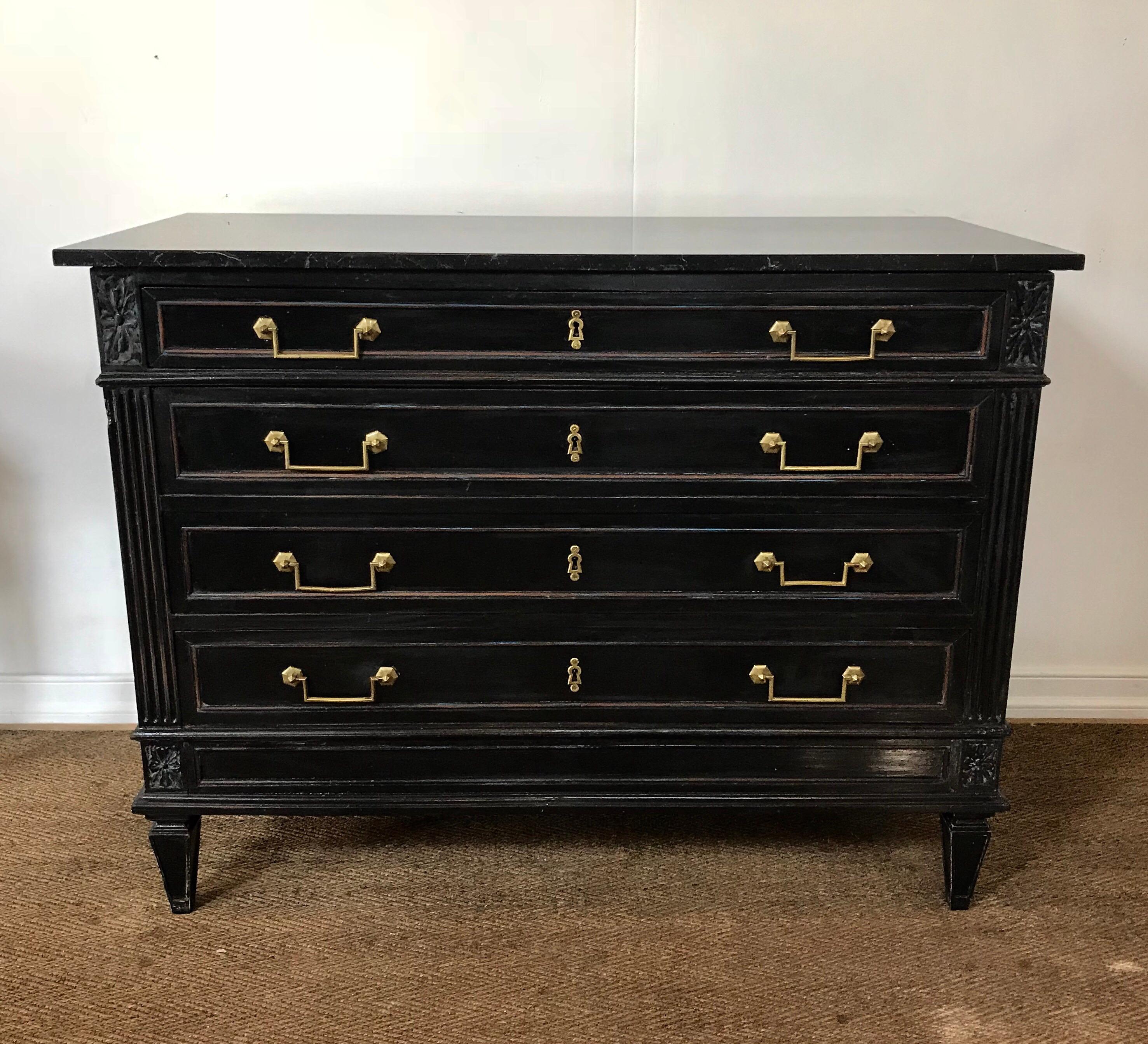 A late 19th century Louis XVI styled marble top commode having a rustic and dusty black ebonized finish complemented by high quality and original brass pulls. The four drawer chest supports a dark charcoal gray granite top which is secondary to the