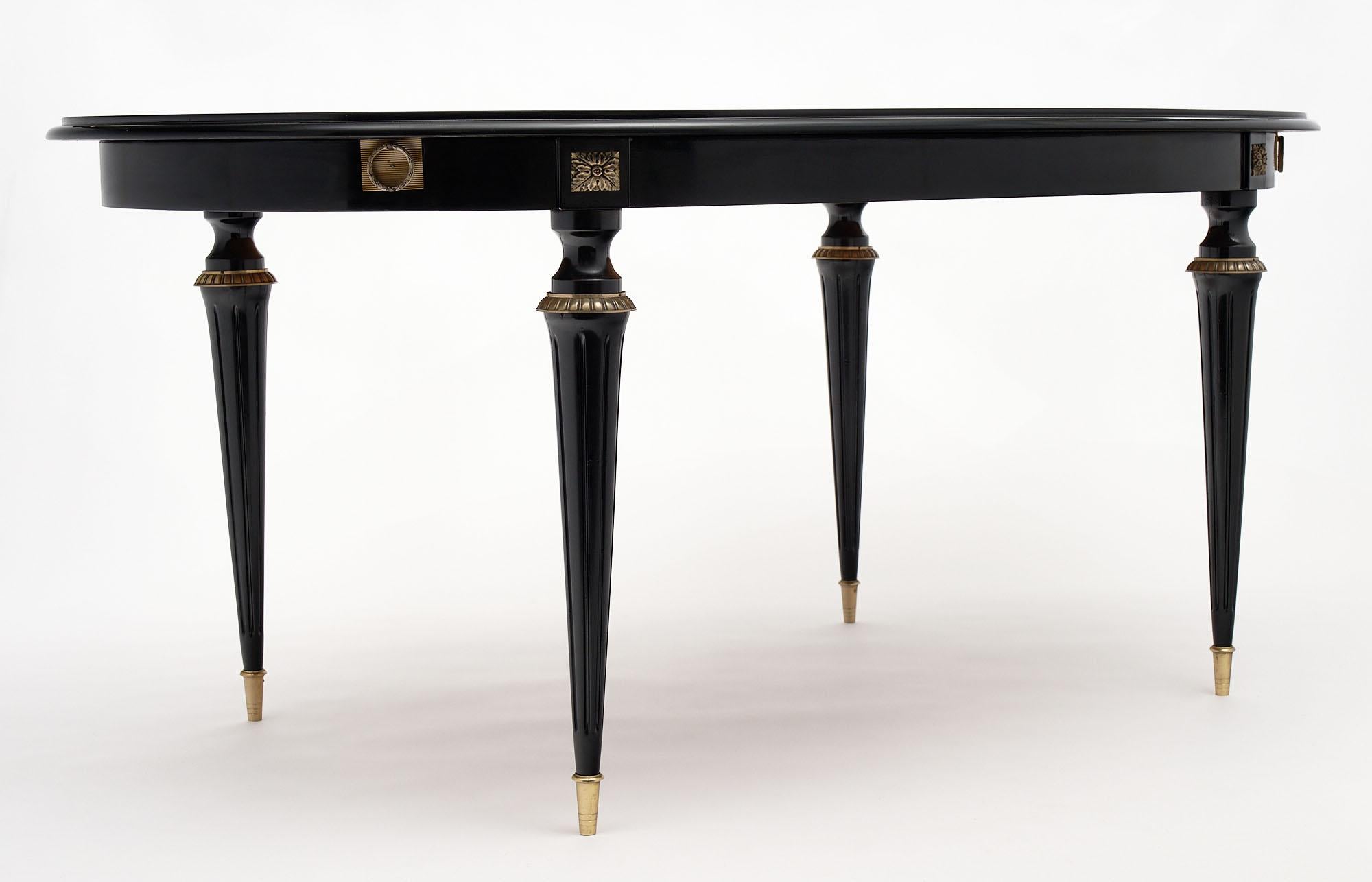 Louis XVI style ebonized oval dining table from France. This piece; made of mahogany and finished in a lustrous museum-quality French polish; has beautiful guilt bronze detail and hand carved fluting on the legs. With leaves that extend an