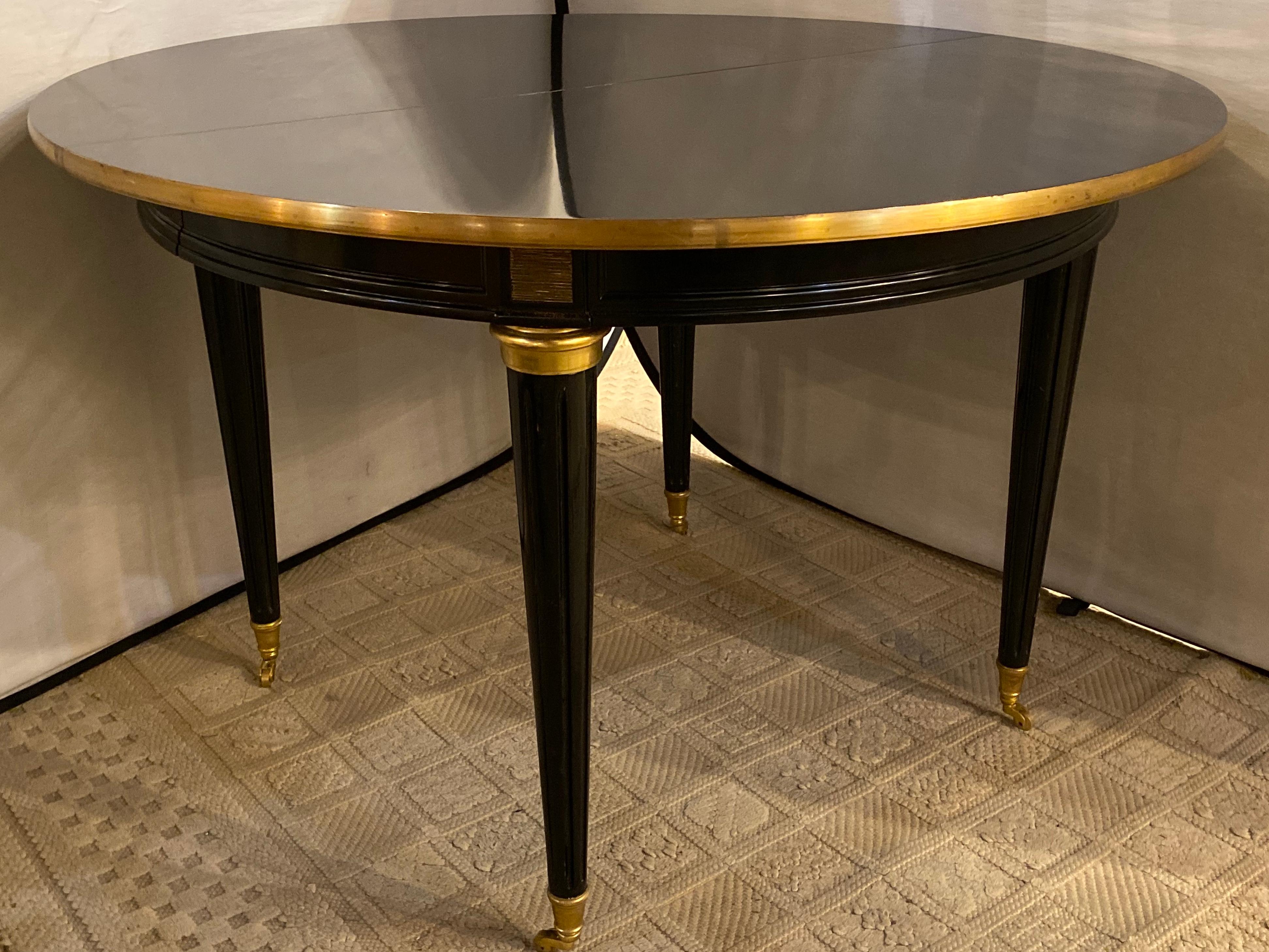 Louis XVI style ebony bronze mounted center or dining table in the manner of Maison Jansen with two 22 inch leaves. This circular Steinway ebony and gilt bronze mounted Hollywood Regency dining or center table is simply stunning. The clean sleek