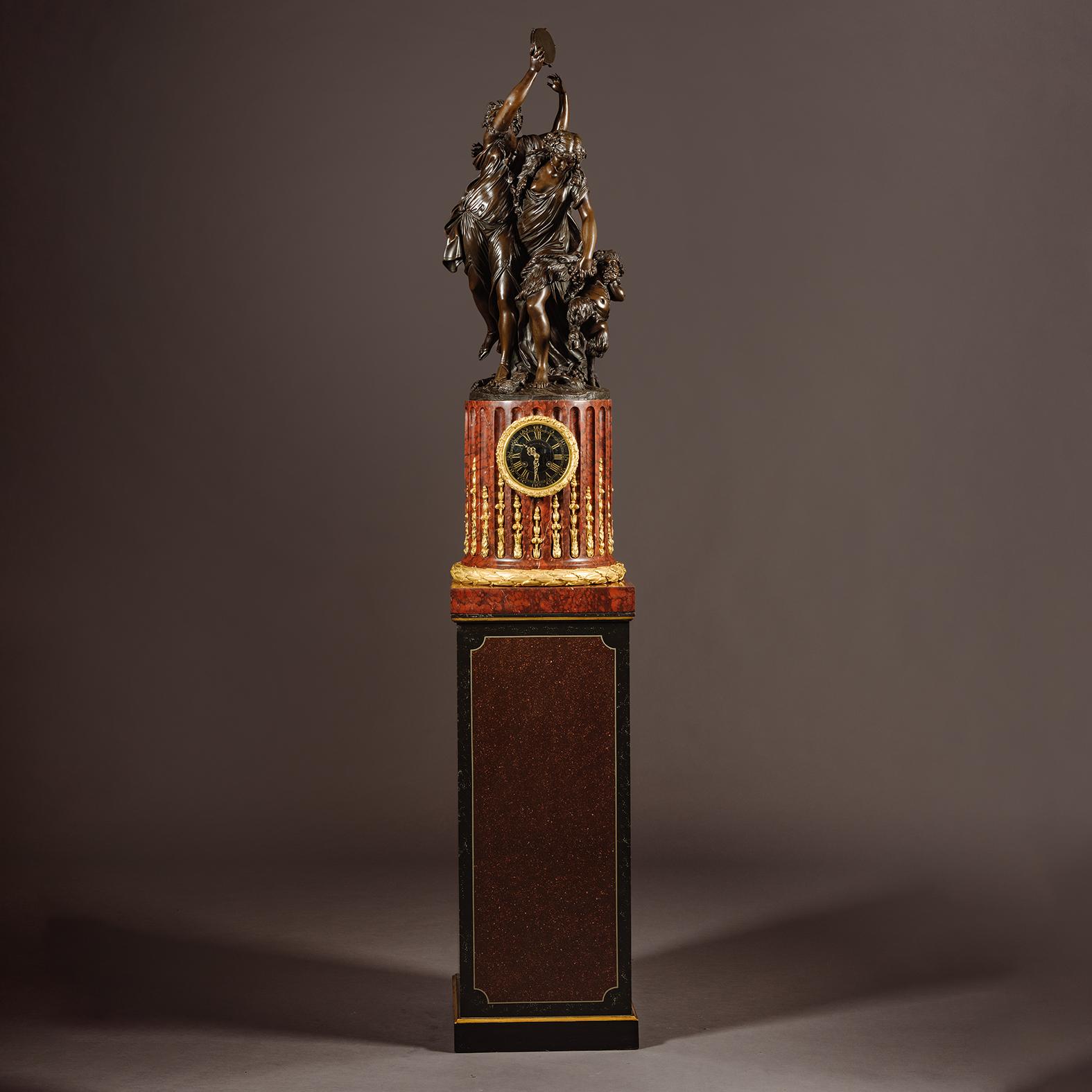 A Large Louis XVI Style Patinated Bronze and Rouge Griotte Marble Figural Pedestal Clock. 

The patinated bronze figural group of Bacchantes is cast from a model by Claude Michel, known as Clodion (French, 1738-1814). It is set atop a Rouge Griotte