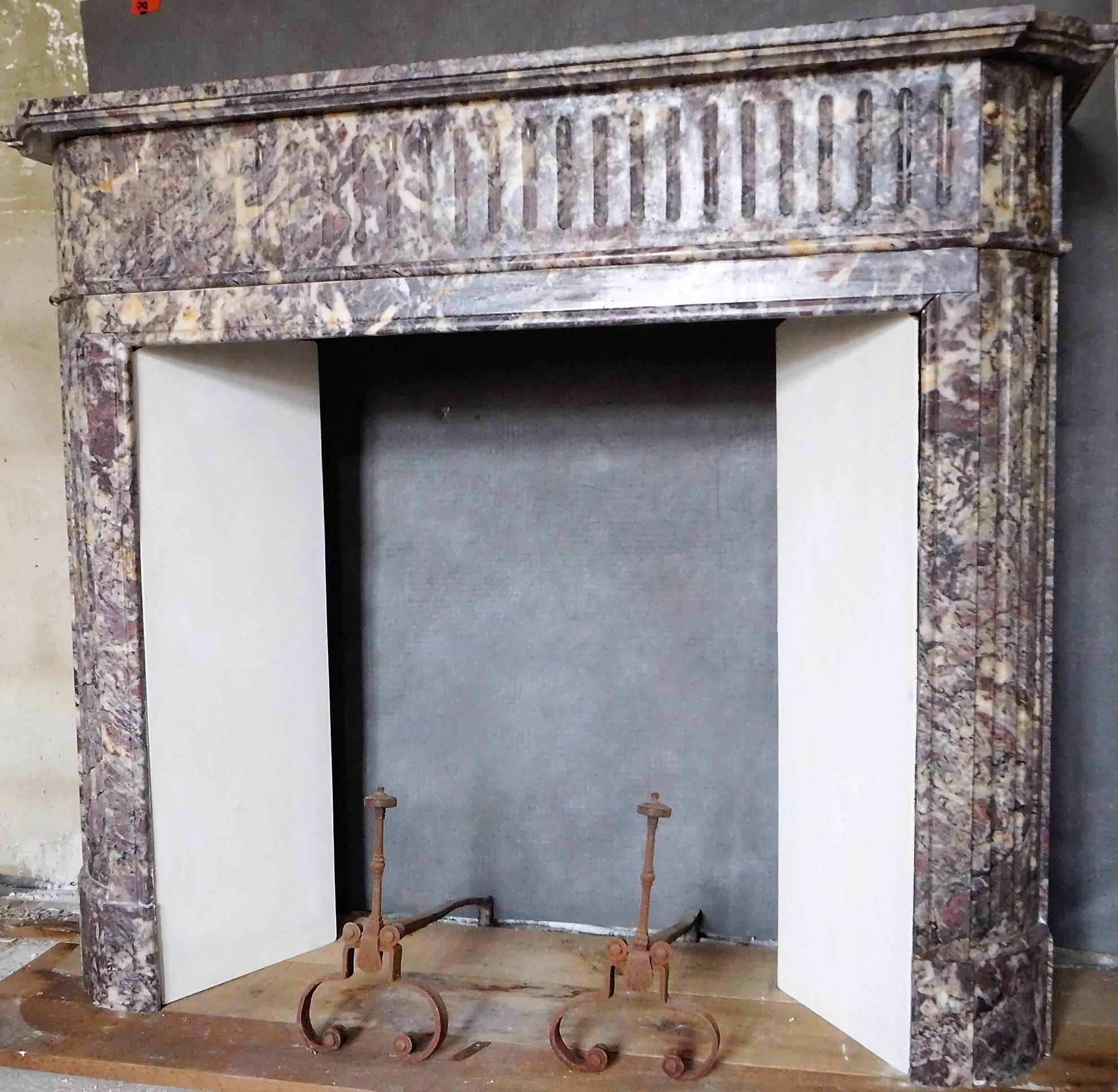 This antique fireplace was made out of the French Brocatelle-Violette du Jura marble, during the second half of the 19th century.
It's nicely decorated with flutes (canelures) on its frieze and jambs.  The expressive colors of this Brocatelle marble