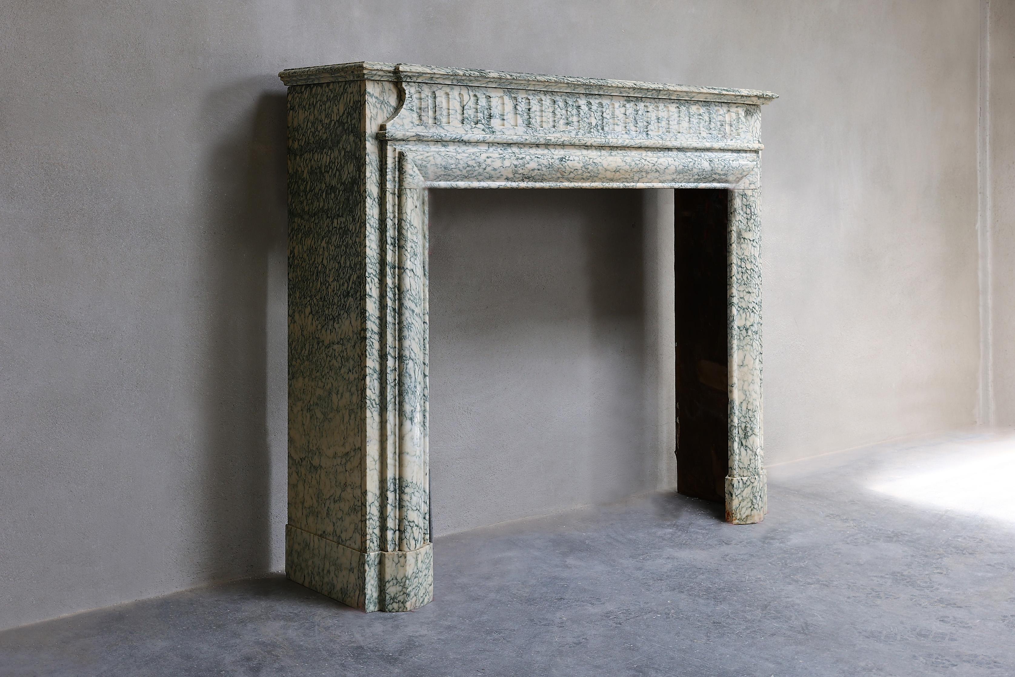An antique fireplace with a straight design and many fluting in the top. The legs are richly decorated with beautiful lines and the size of this Vert d'estours marble fireplace is compact and suitable for many interiors.