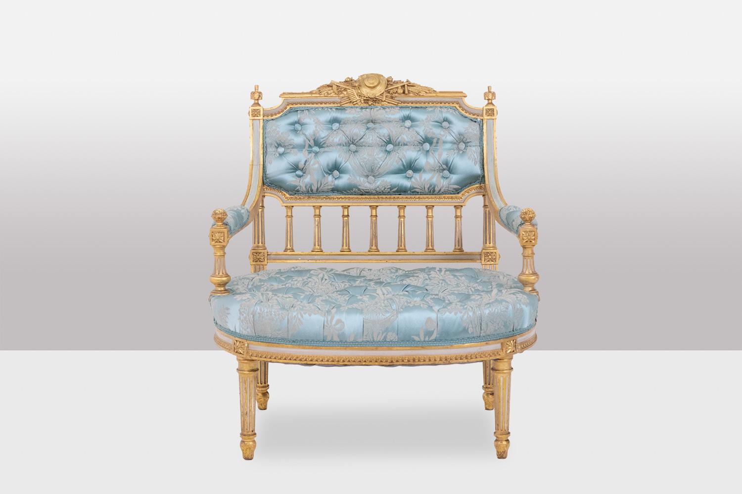 Louis XVI style fireside chair in gilded and lacquered wood. Padded seat, backrest and cuffs, the top of the backrest decorated with the attributes of music, connecting dice decorated with stars, decoration of columns between the seat and the