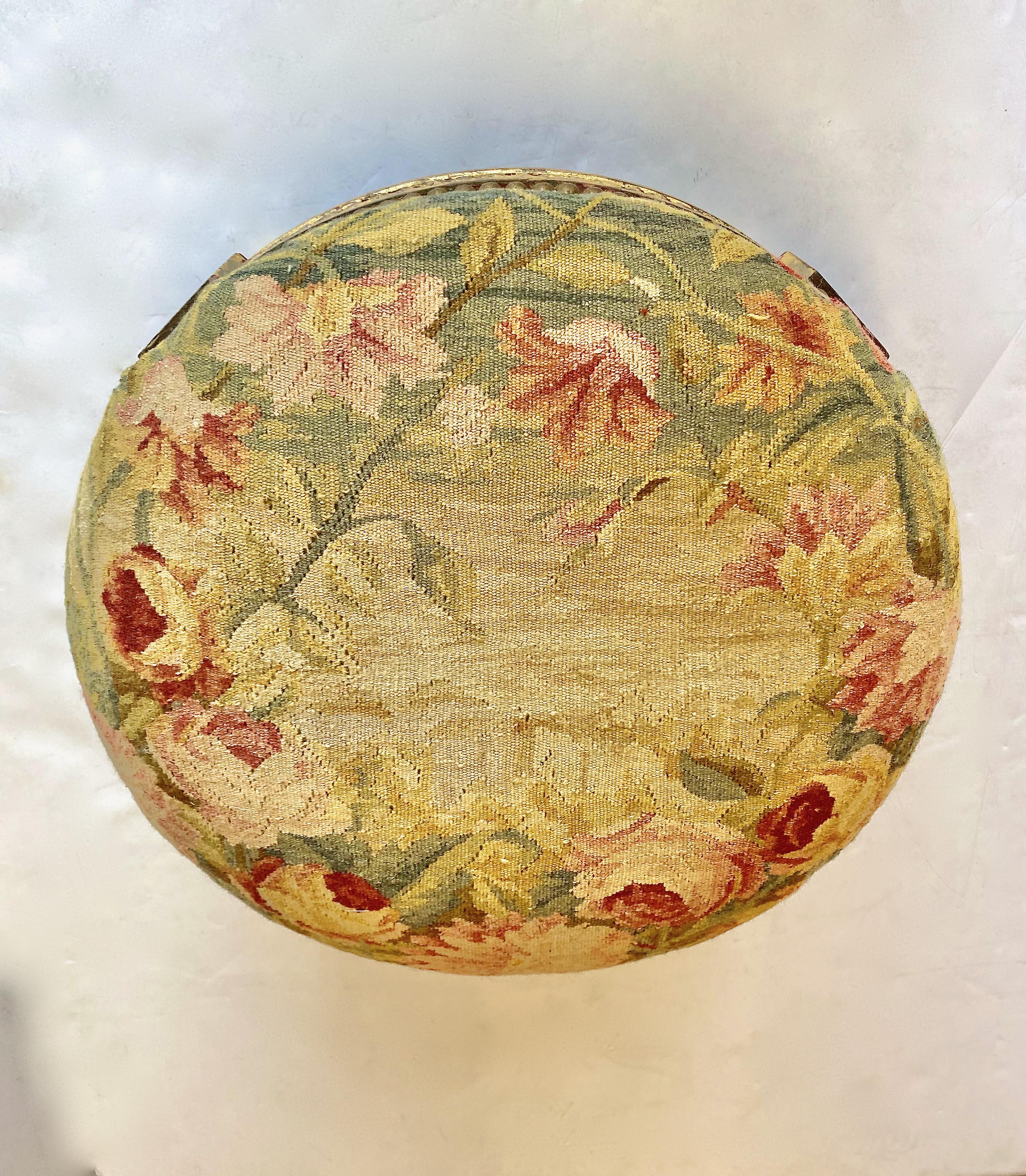 This is a charming little footstool in the style of Louis XVI. The carved wood frame is highlighted with gold leaf. The seat or footrest is covered in an antique floral Flemish or French tapestry fragment. This is a sexy little stool and it is ready