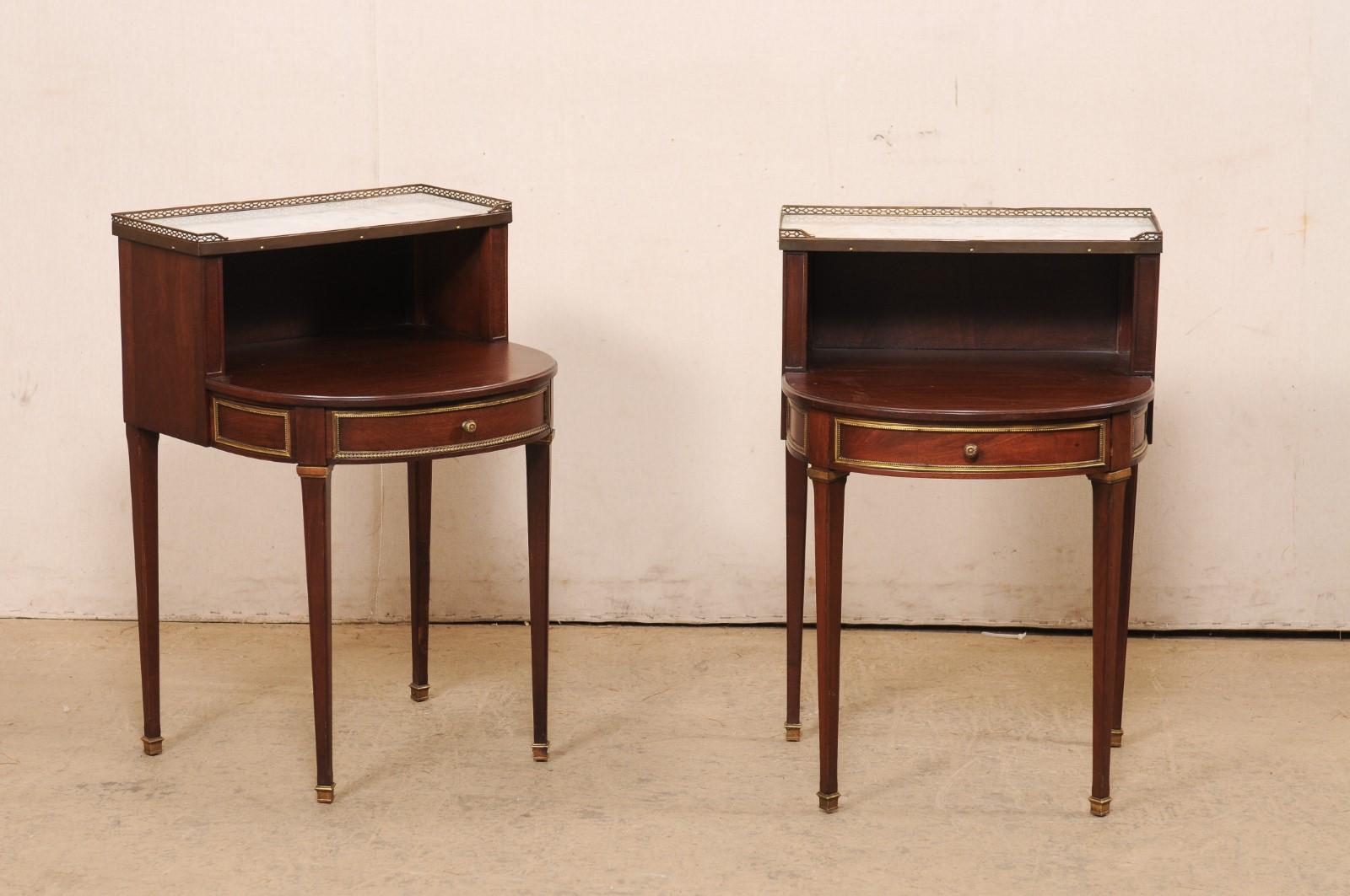 A French pair of Louis XVI style wood end tables, with marble and brass, from the 20th century. This vintage pair of petite sized tables from France, designed in Louis XVI style, each feature a rectangular-shaped white marble top, surrounded with a