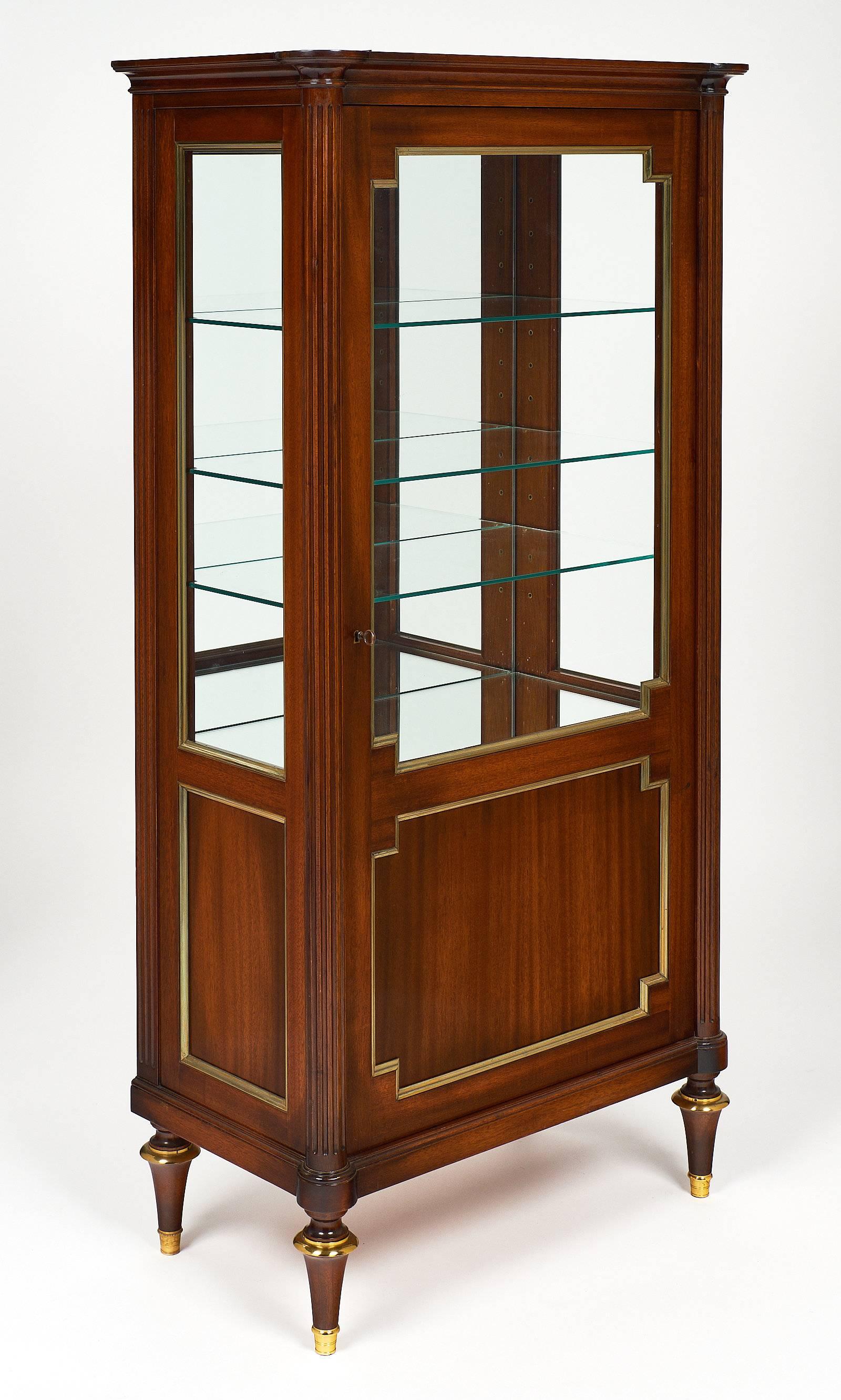 French antique Louis XVI style bookcase / vitrine ”bonnetiere.” This piece is made of mahogany. It has one door with beveled glass and a working lock and key. The mirrored interior boasts three adjustable glass shelves. Gilt brass trims are found