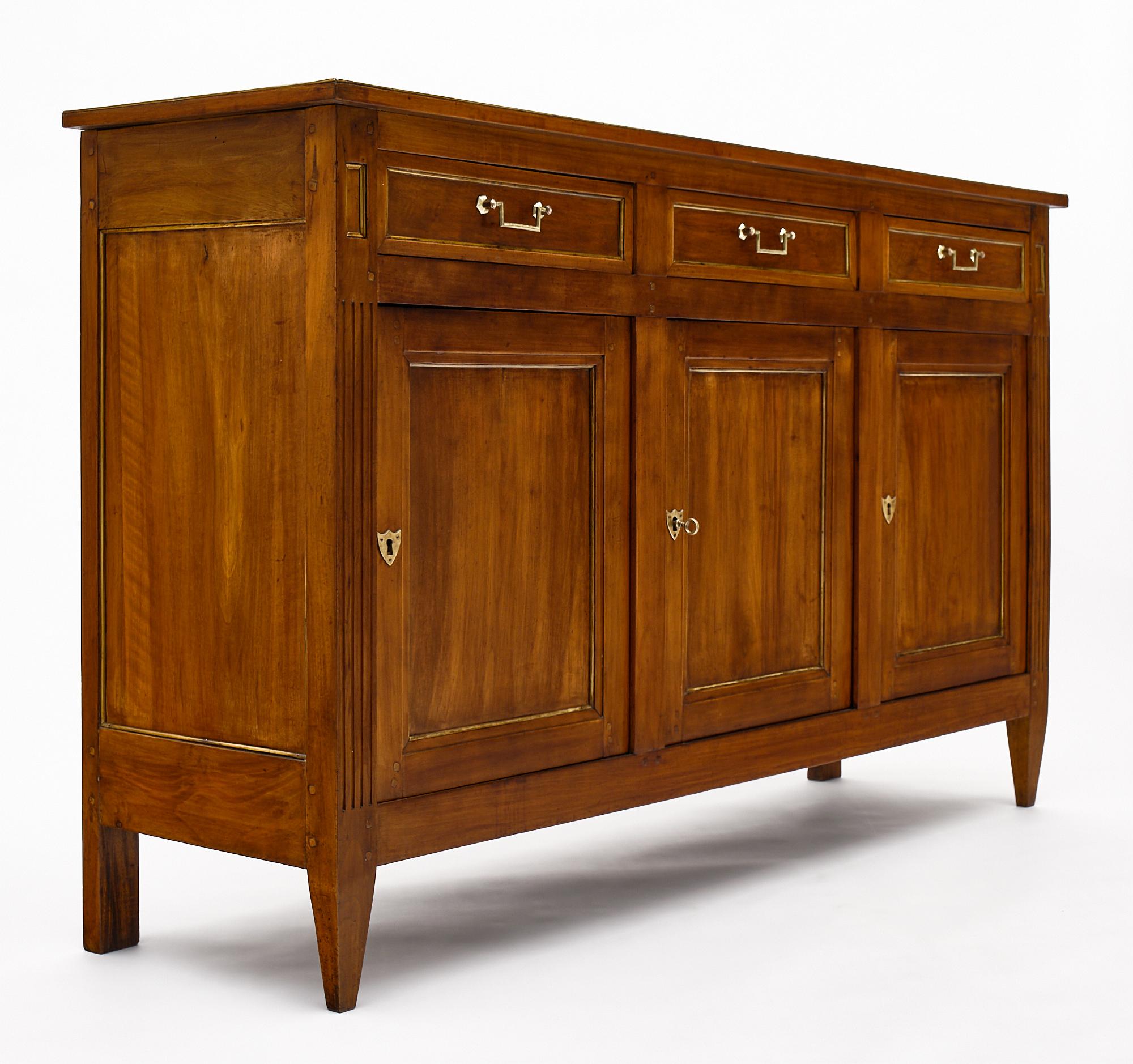 Louis XVI style French antique buffet made of solid walnut and finished with a bees wax. There are three dovetailed drawers above three doors all featuring gilt brass trim, bronze hardware, and interior adjustable shelving. A lovely, inviting piece!