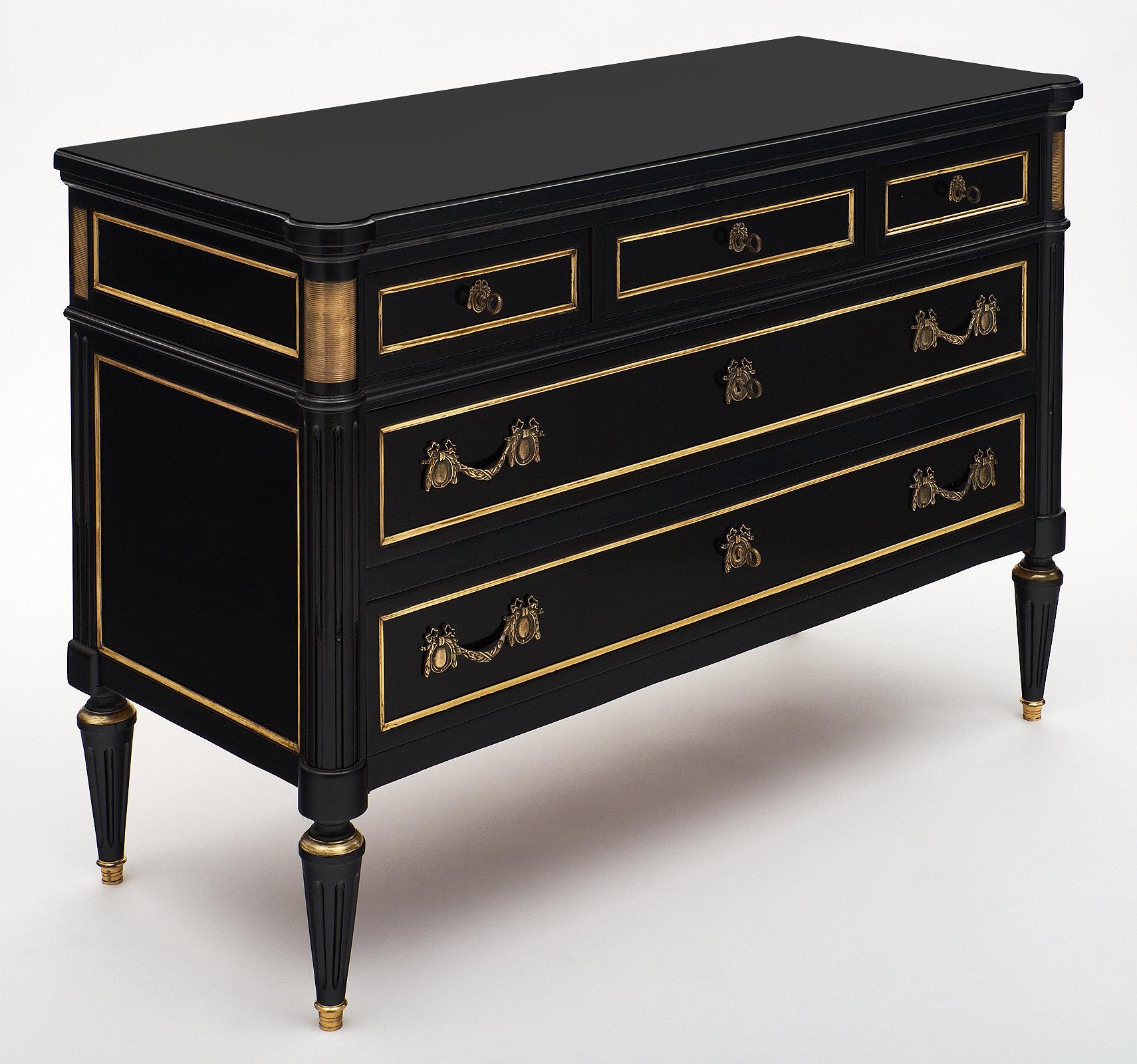 A French antique Louis XVI style chest of drawers featuring five dovetailed drawers and finely cast hardware. This piece is made of ebonized mahogany, finished with a lustrous French polish. We love the gilt trims throughout. This elegant “commode”