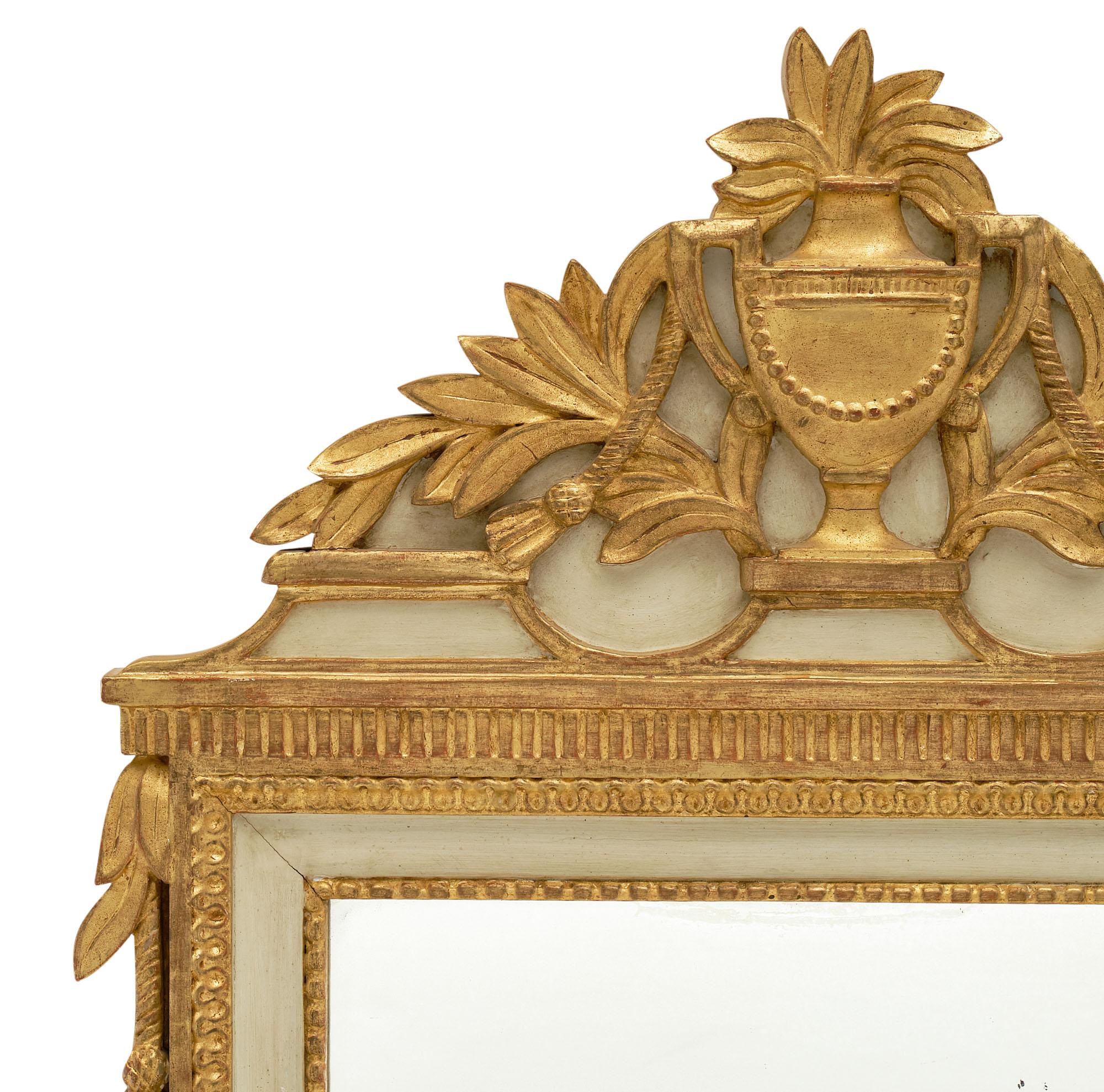 Louis XVI style French antique mirror with intricate decor of a classical urn and laurel branches. The 23 carat gold leaf and original light almond green paint finish give this such a classic and beautiful look. It is all original.