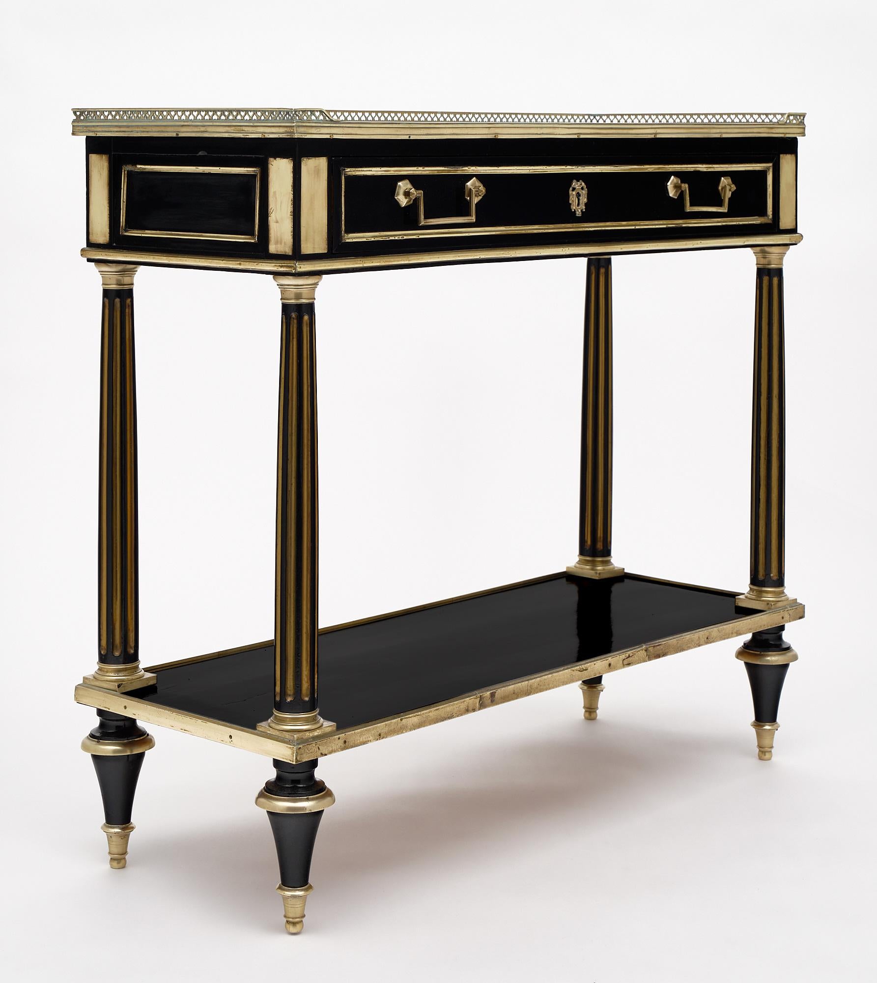 Louis XVI style French console table in the Louis XVI style made of mahogany and finished with gilt brass details throughout. This piece is ebonized and has a hand-rubbed French polish. The top is mirrored and we love the functional shelf below.
