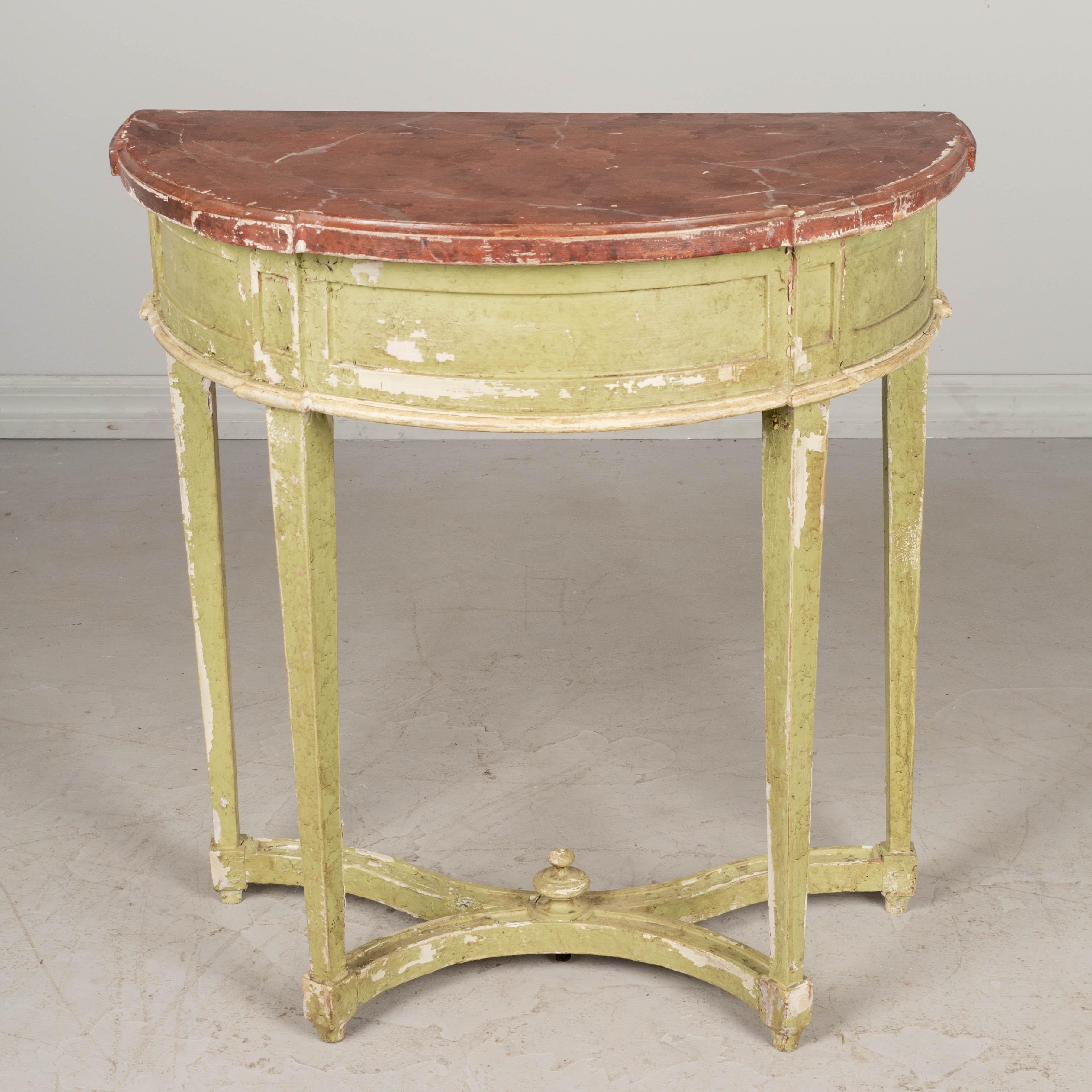 A Louis XVI style French demilune wood console table with pale green painted finish and realistic looking faux painted red marble top. Tapered legs supported by a curved stretcher with small turned finial decoration. Original finish with some