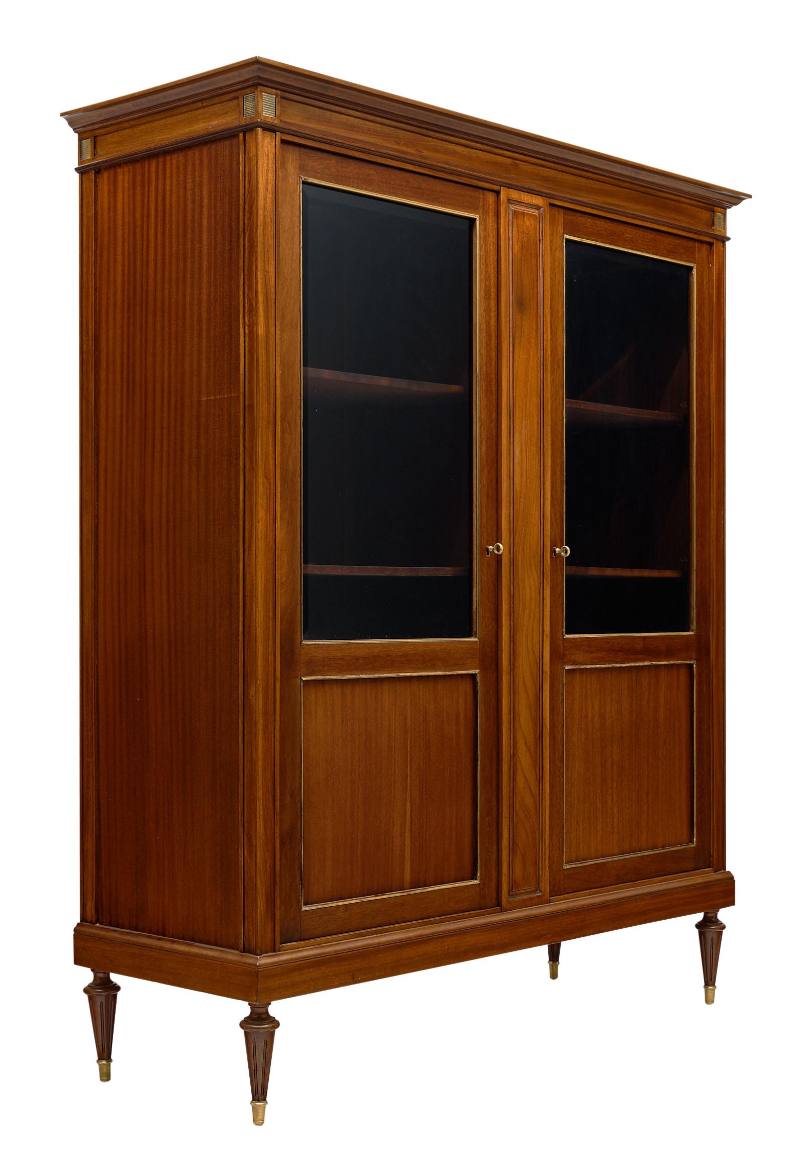 Louis XVI style French mahogany bookcase with wonderful brass trim throughout and interior shelving to house your priceless collectables or book collection. We love the warmth of the mahogany and the strong; Classic details and proportions.