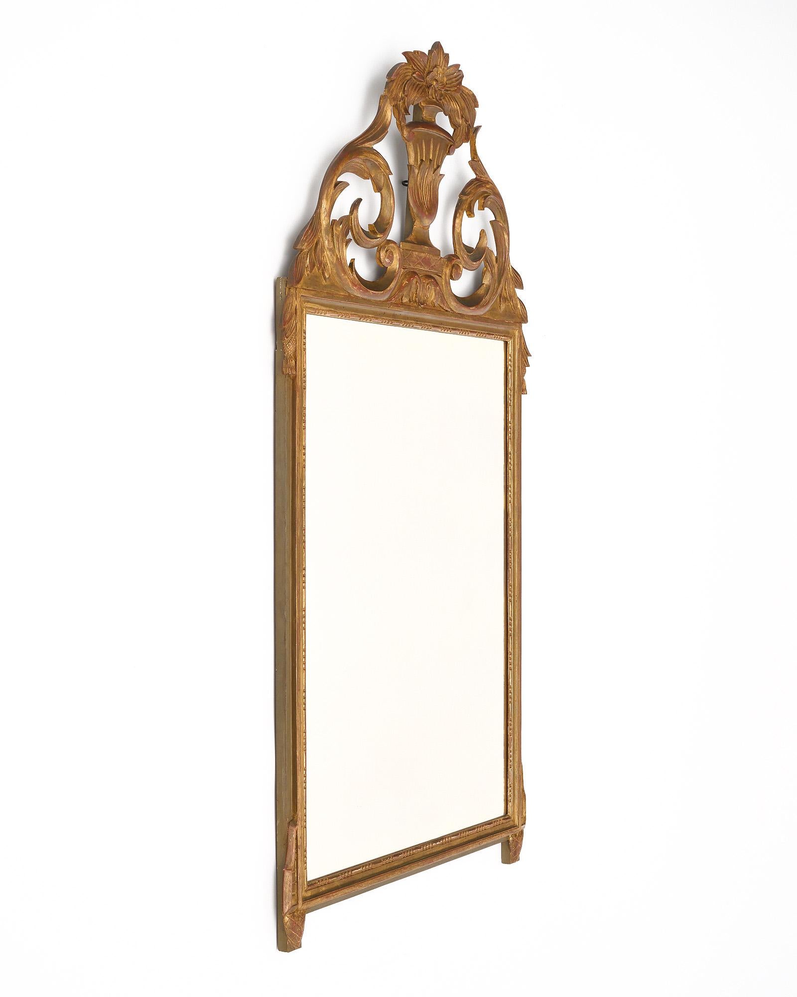 Mirror from France in the Louis XVI style. This piece is made of stuccoed hand-carved wood with a fronton that features an urn, floral motifs, and laurel leaves. The 24 carat gold leafing is original. Some repairs have been made to the frame.