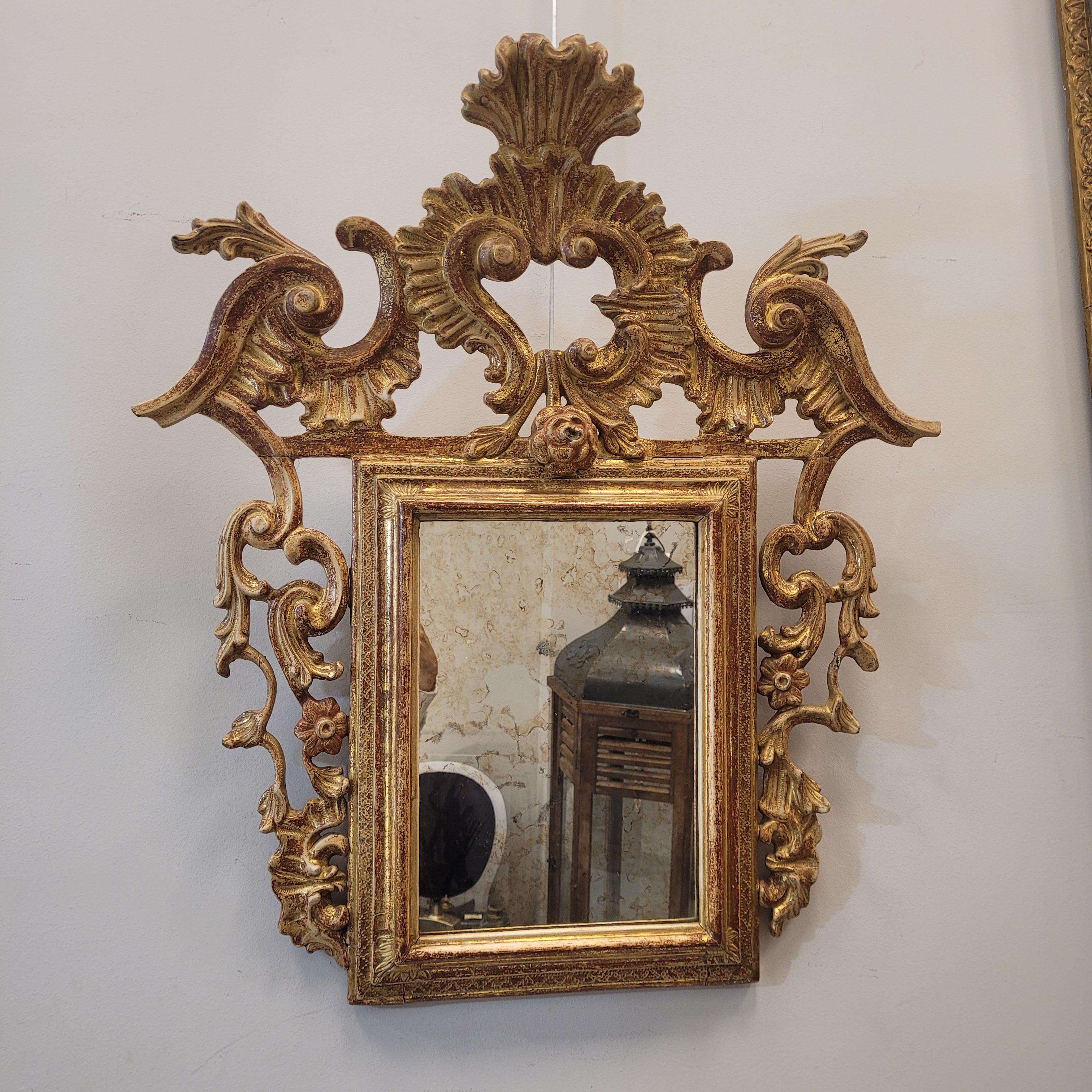 Eccezionale  specchio in legno intagliato e dorato, realizzato nel primo quarto del XX secolo in stile Luigi XVI. Lo specchio argentato è incorniciato in un corpo principale rettangolare. In cima c'è una cresta rigogliosa, sottile e leggera, che