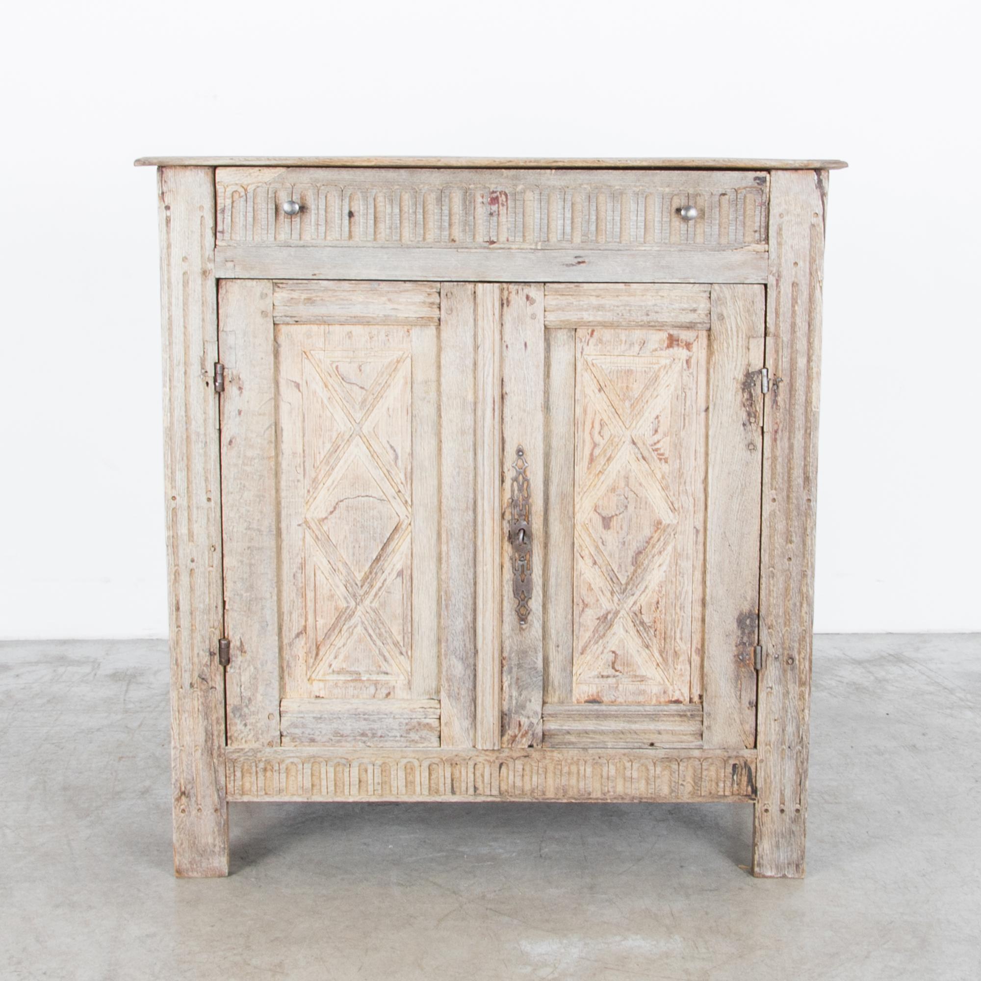 An oak buffet from France, circa 1860, featuring two doors which open onto an interior shelf. The simple silhouette is embellished by provincial carvings in pretty, geometric patterns, including a harlequin motif on the door panels, and an elaborate