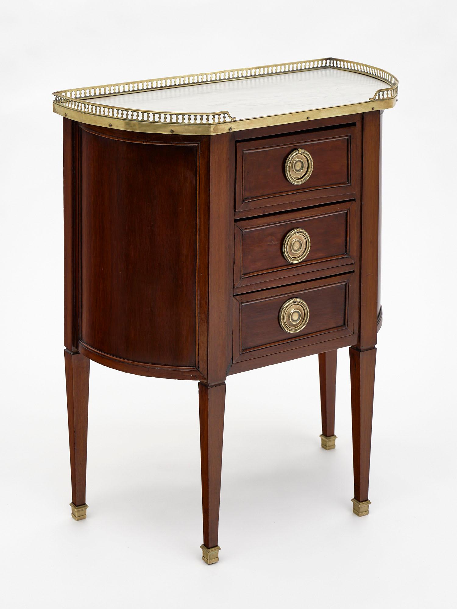 Louis XVI style French petite chest or side table made of walnut and featuring three dovetailed drawers. It is topped with Carrara marble accented with an open; gilt brass gallery. We love the finely cast bronze medallion hardware. Such a lovely